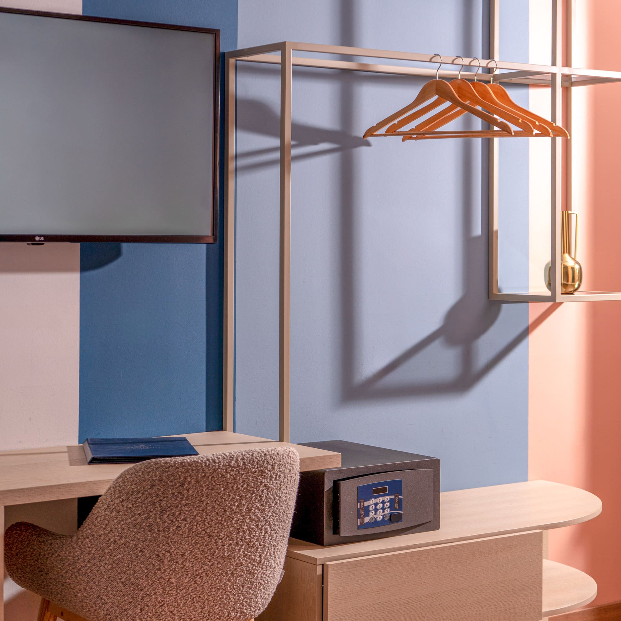 Modern hotel room interior: desk, TV, open wardrobe with hangers, and safe.