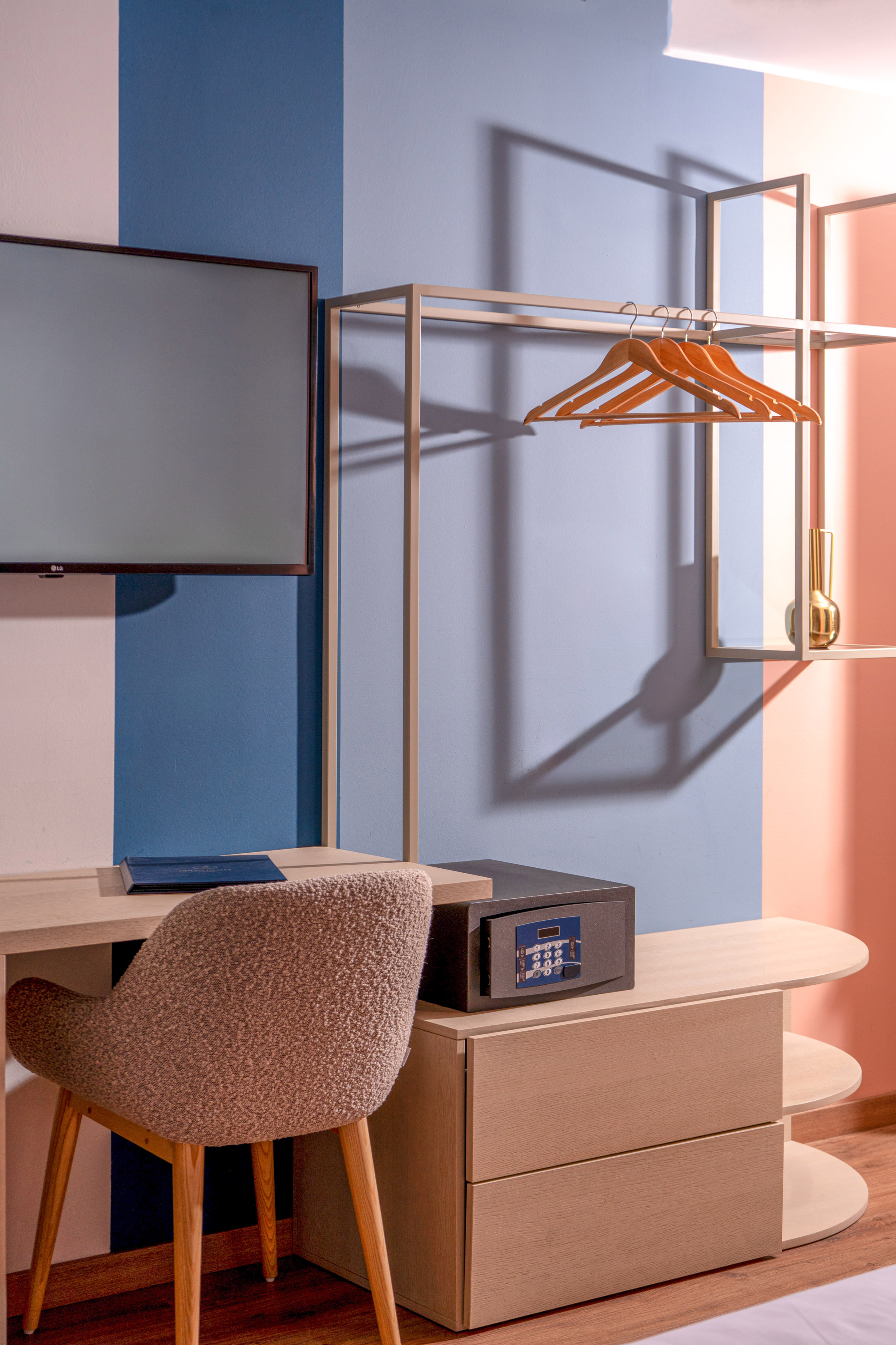 Modern hotel room interior: desk, TV, open wardrobe with hangers, and safe.