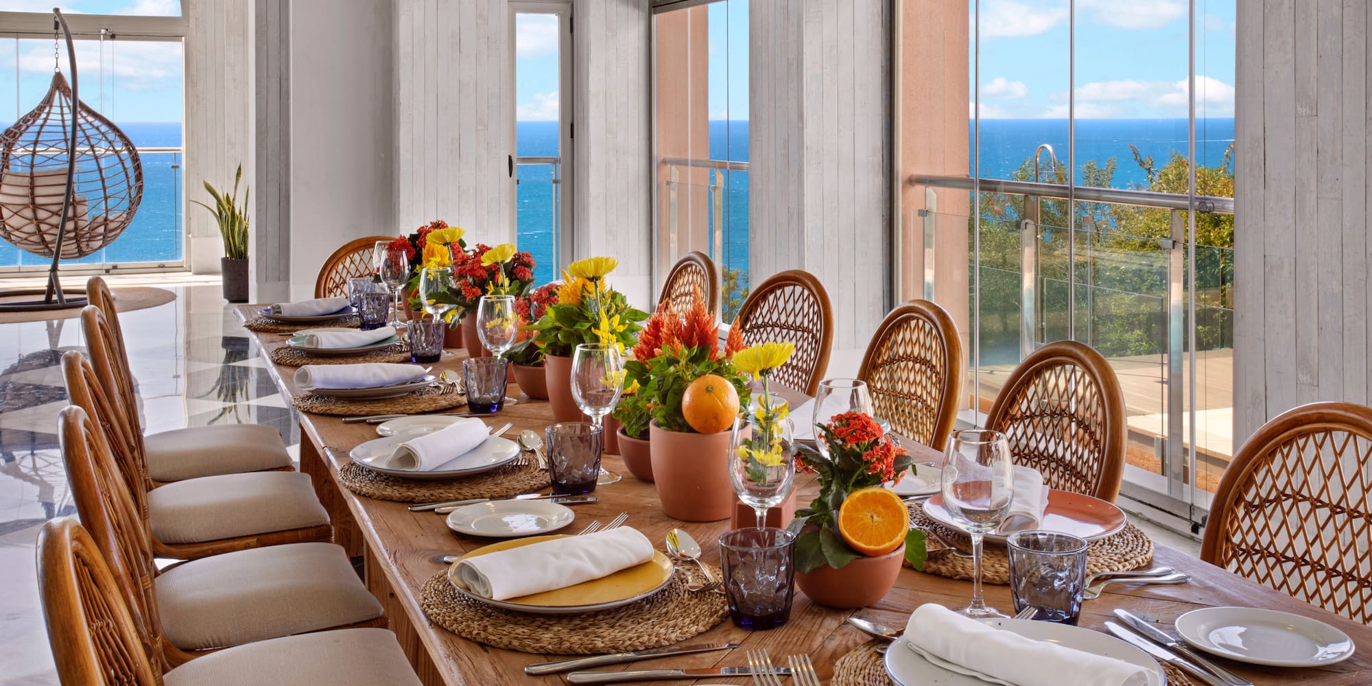 Dining table set with flowers, wicker chairs, and expansive ocean view.
