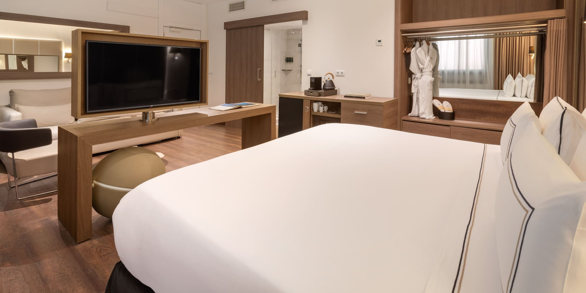 Hotel suite with king bed, TV, lounge area, and wooden wardrobe.