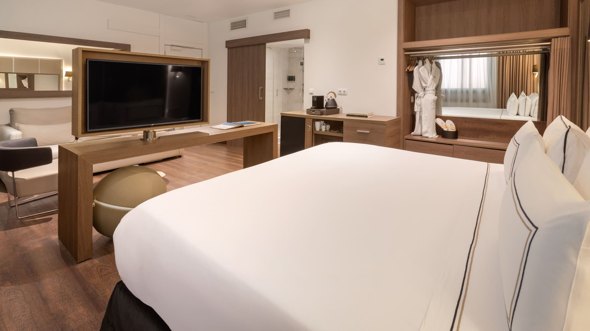 Hotel suite with king bed, TV, lounge area, and wooden wardrobe.