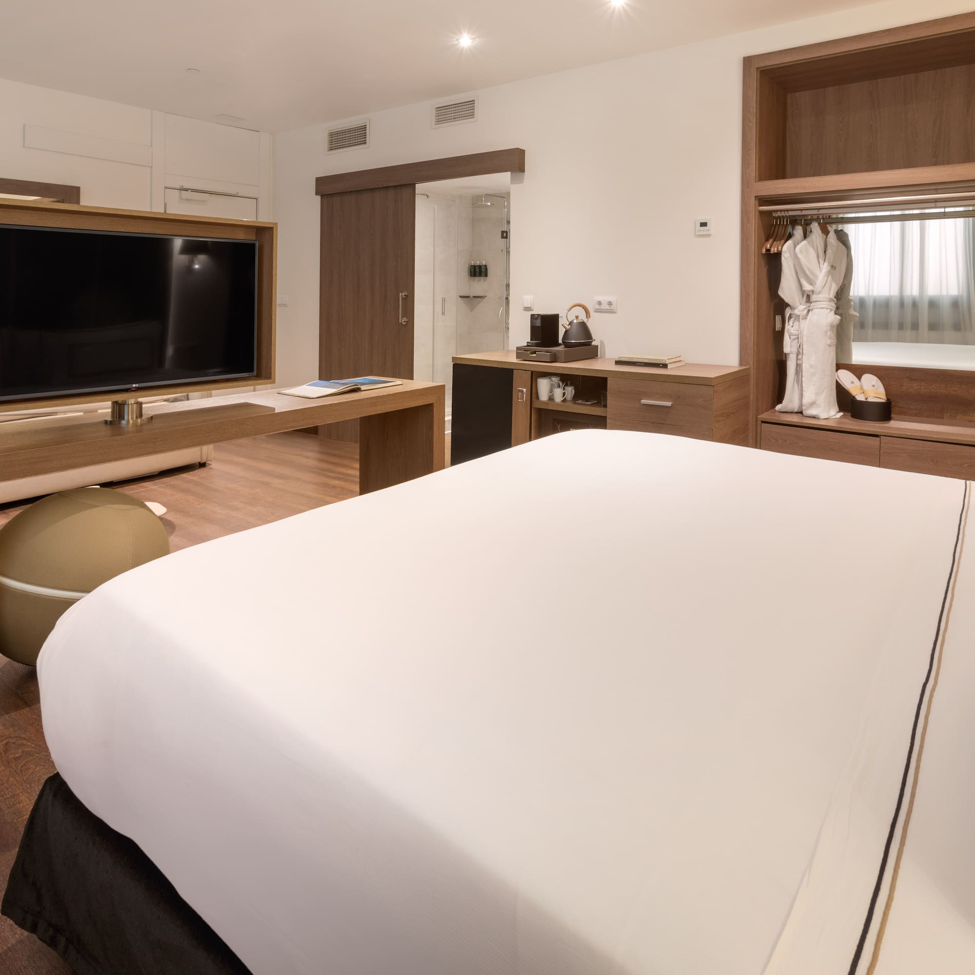 Hotel suite with king bed, TV, lounge area, and wooden wardrobe.
