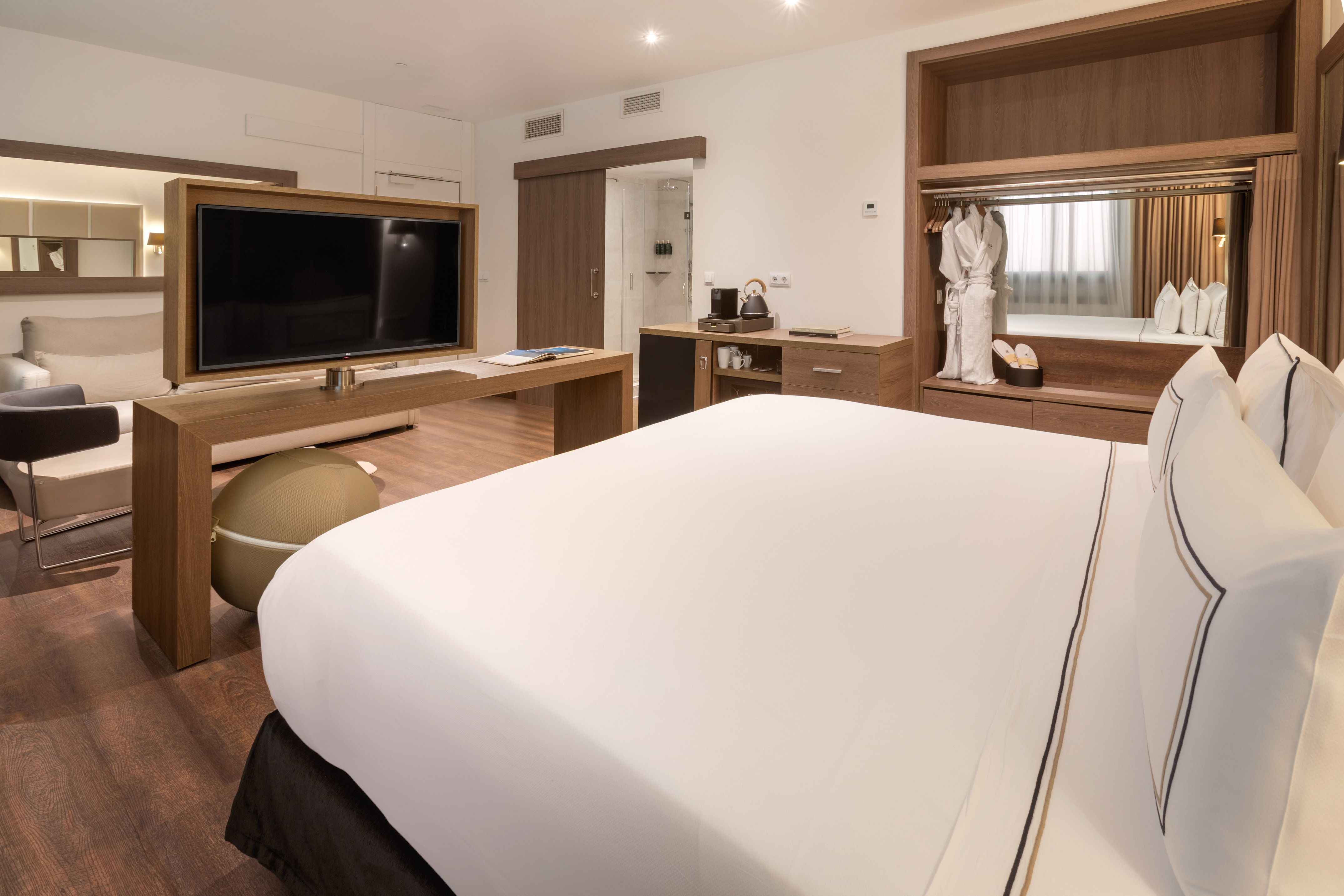 Hotel suite with king bed, TV, lounge area, and wooden wardrobe.