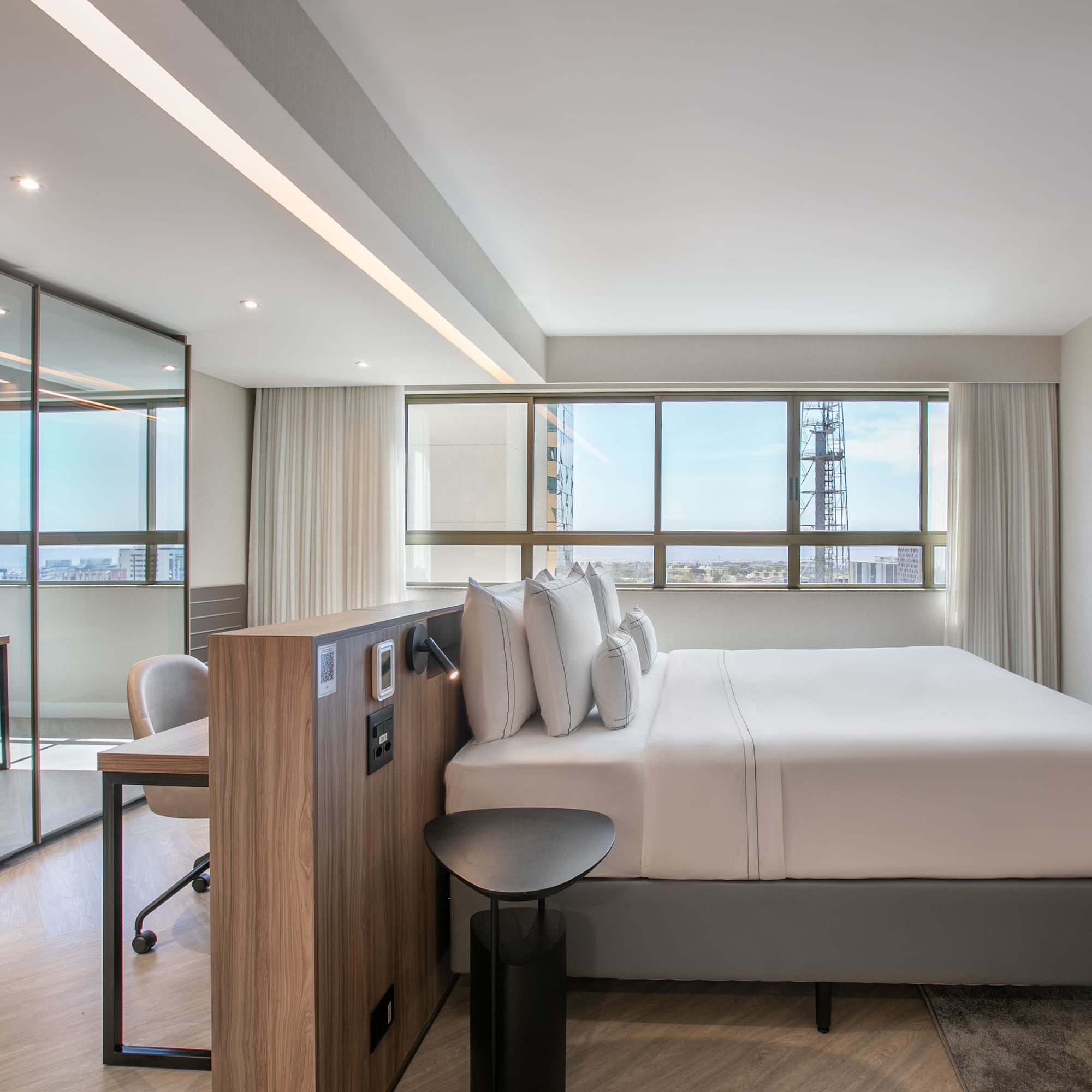 Modern hotel suite with king bed, city view, and glass-partitioned workspace.