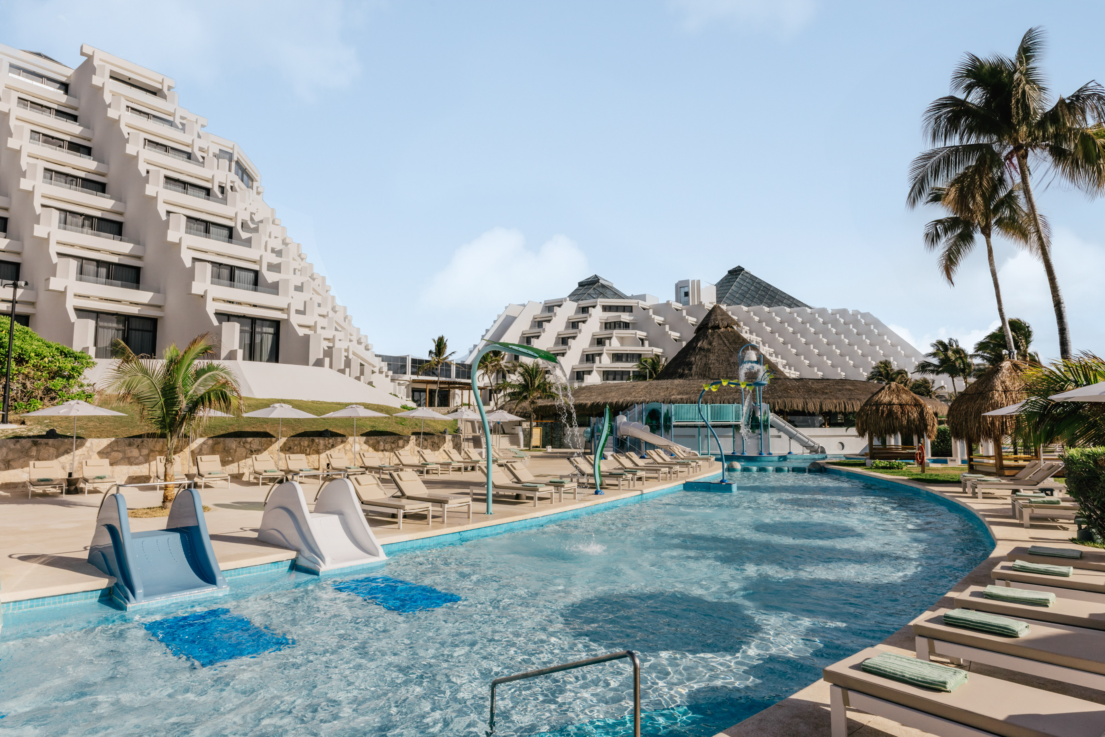 Resort water park pool with slides, lounge chairs, and tiered hotel architecture.
