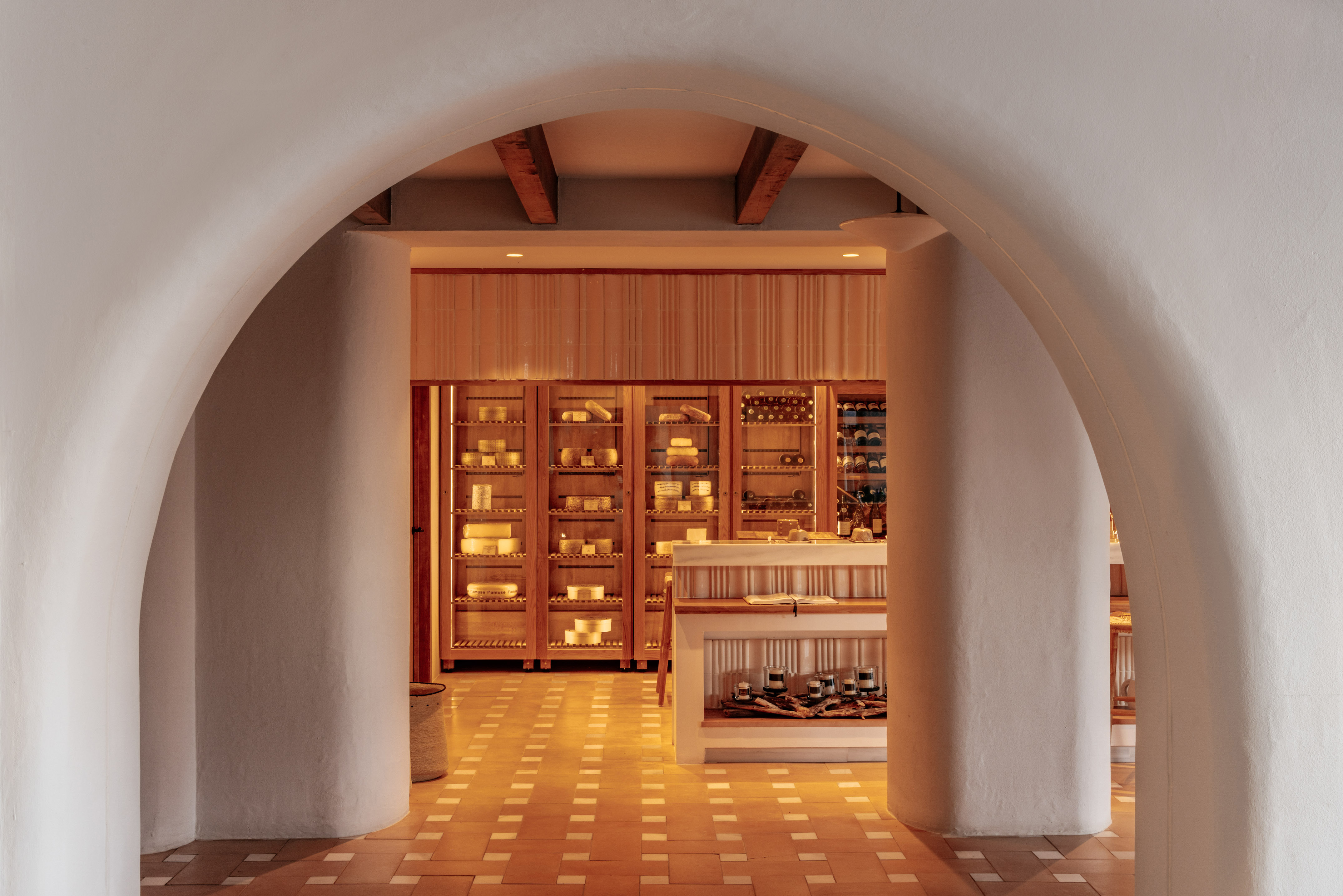 Arched entrance to a cheese shop with wooden display cabinets and tiled floor.