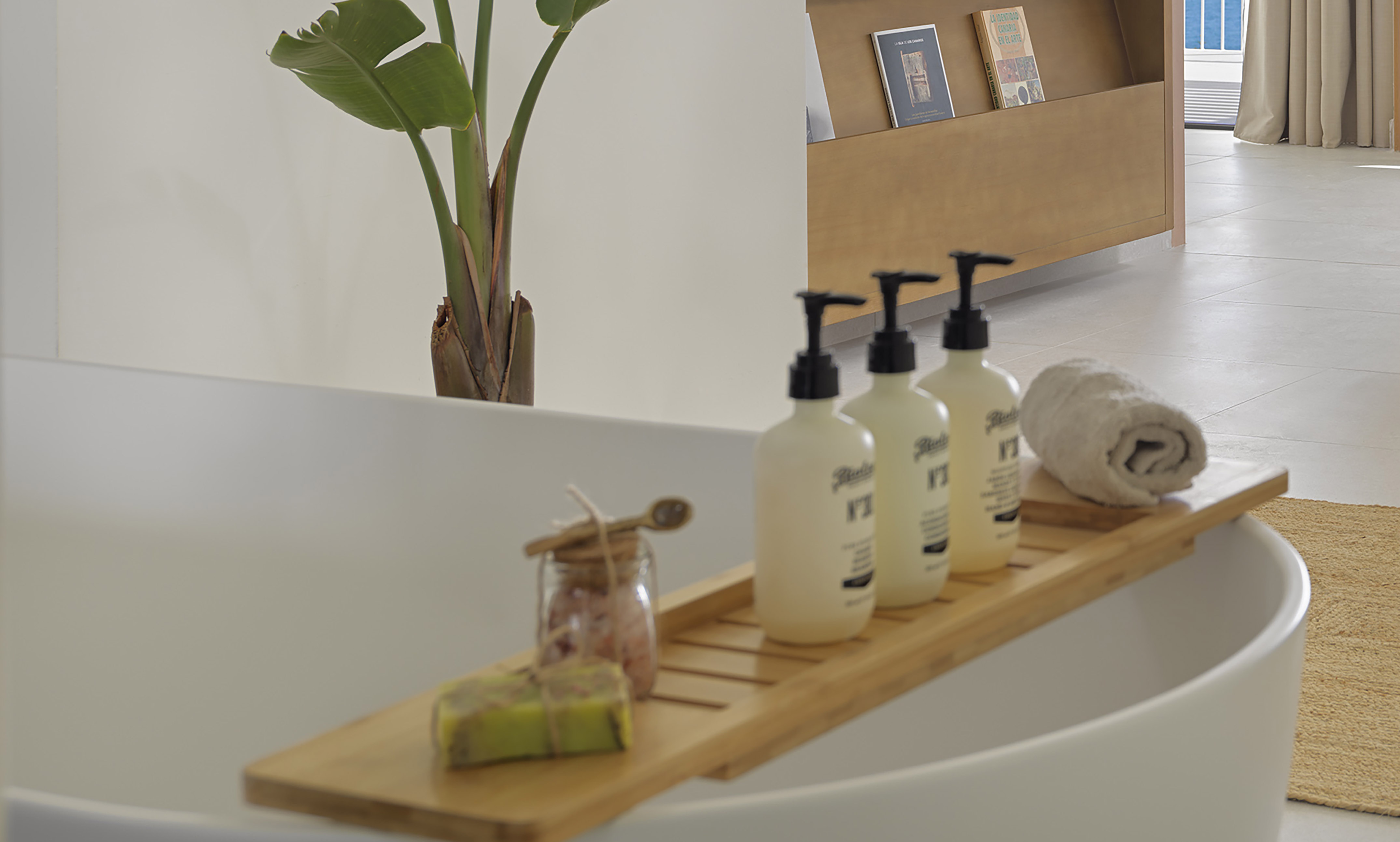 White bathtub with wooden bath caddy, spa toiletries, towel, and plant.