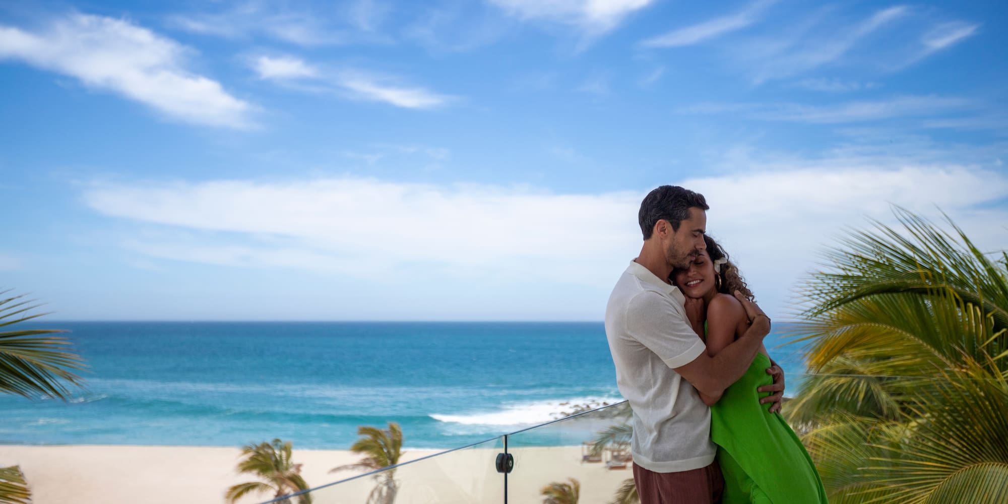 a man and woman hugging on a balcony overlooking a beach