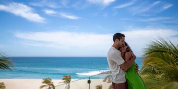 a man and woman hugging on a balcony overlooking a beach