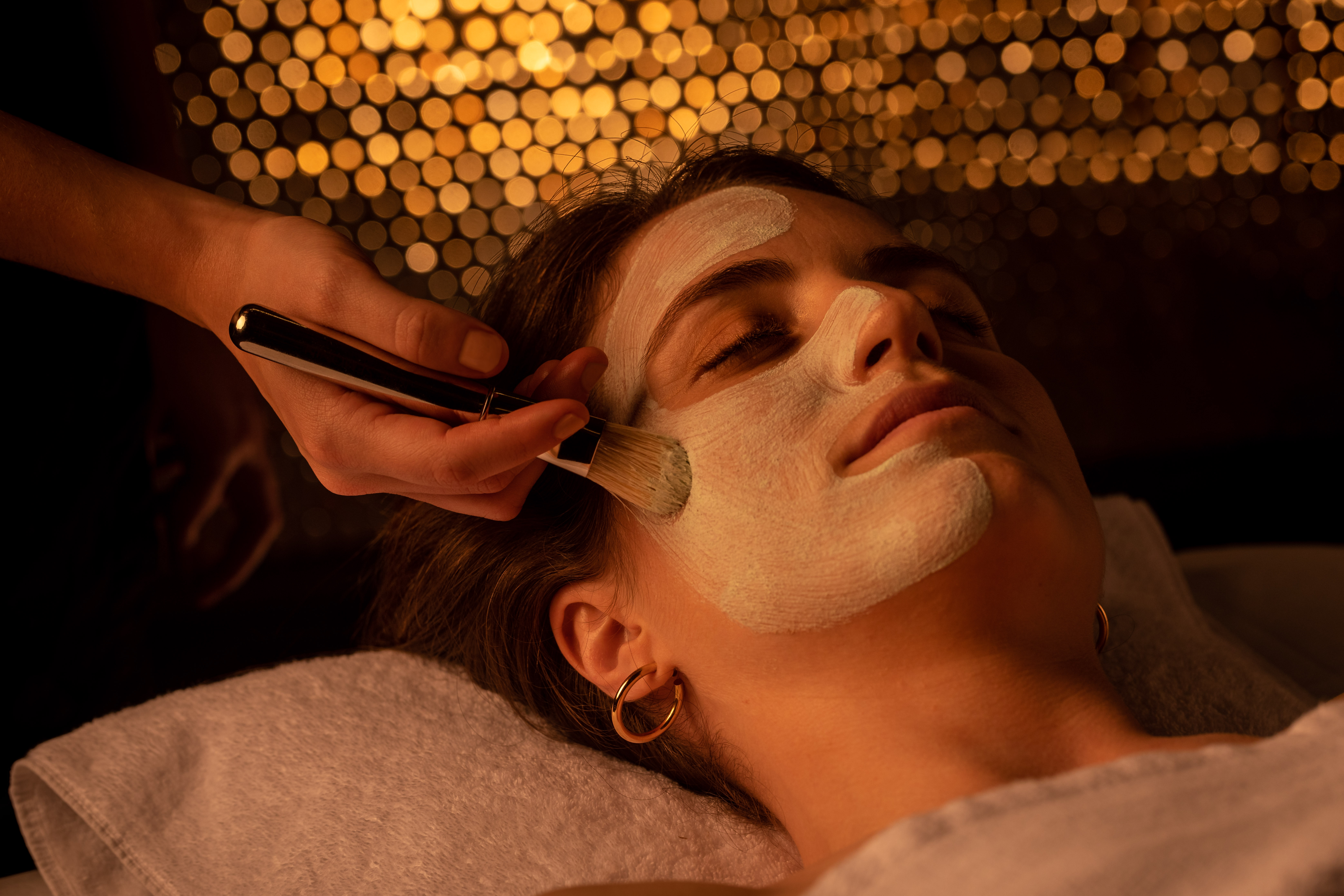 a person applying a white mask on a woman's face