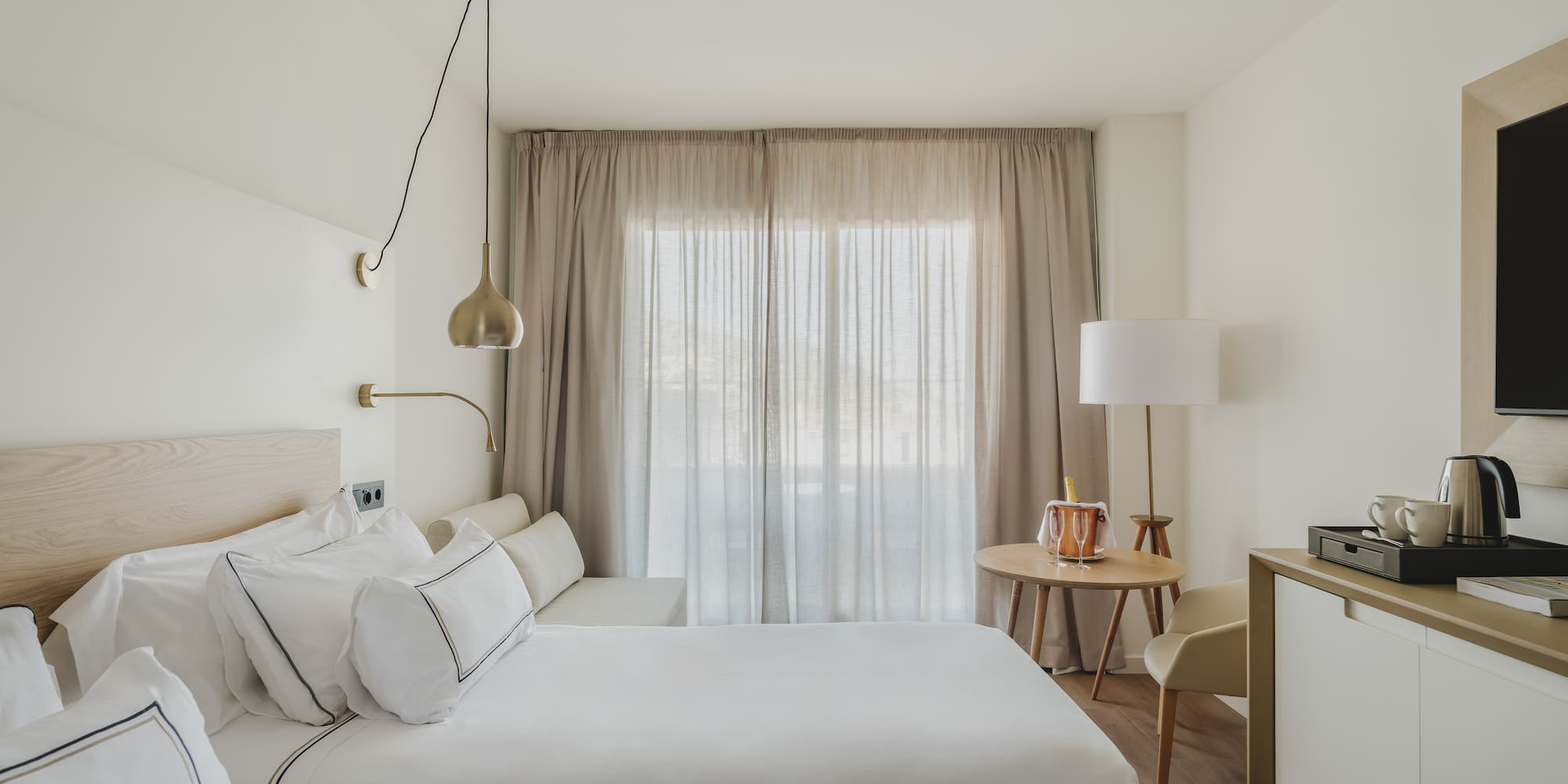 Habitación doble de hotel moderna, tonos neutros, camas y ventanal con cortinas.