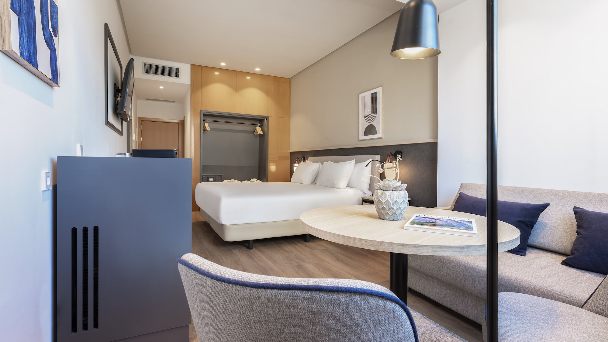 Modern hotel room with bed, sofa, wooden floor, and contemporary decor.
