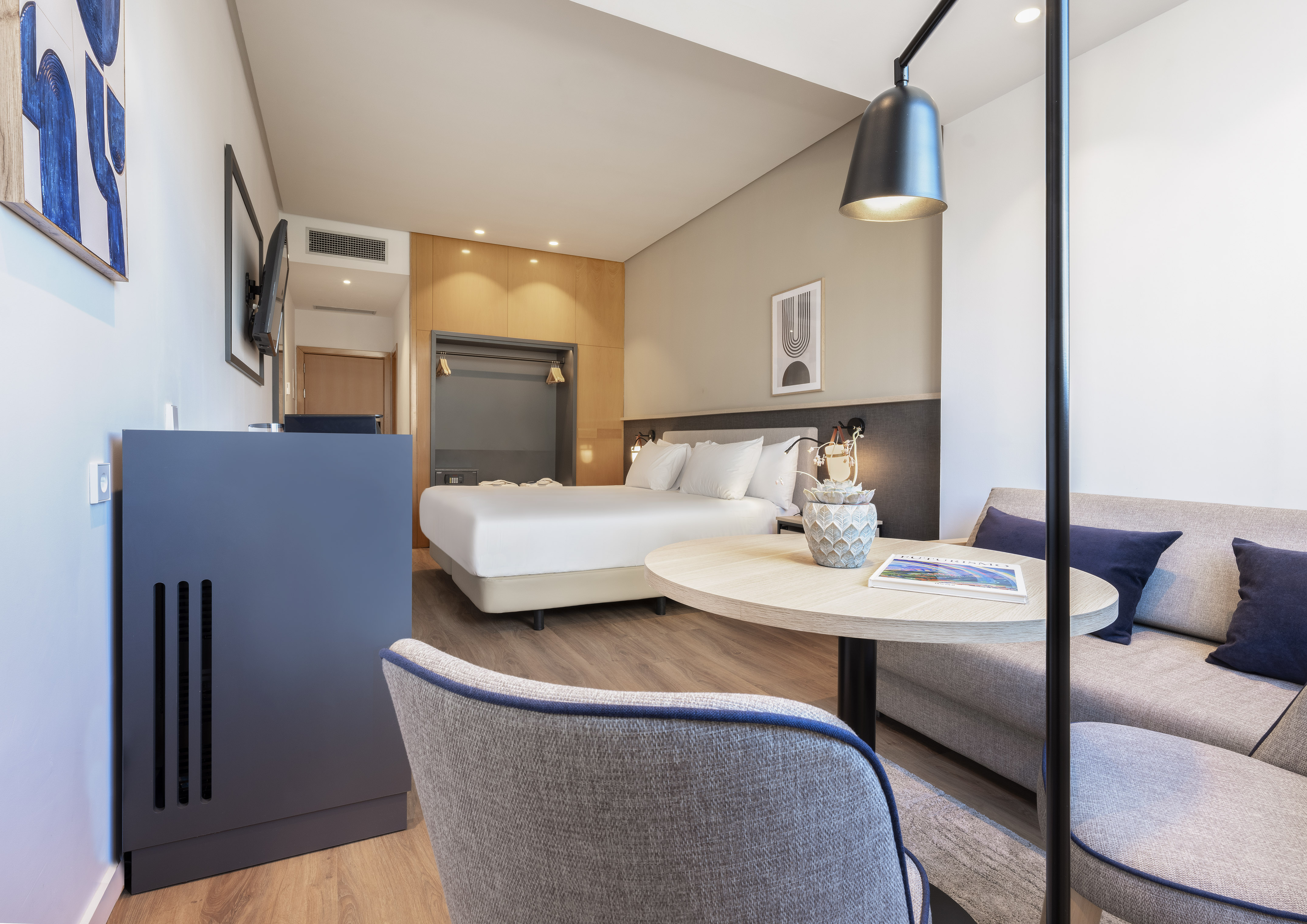 Modern hotel room with bed, sofa, wooden floor, and contemporary decor.