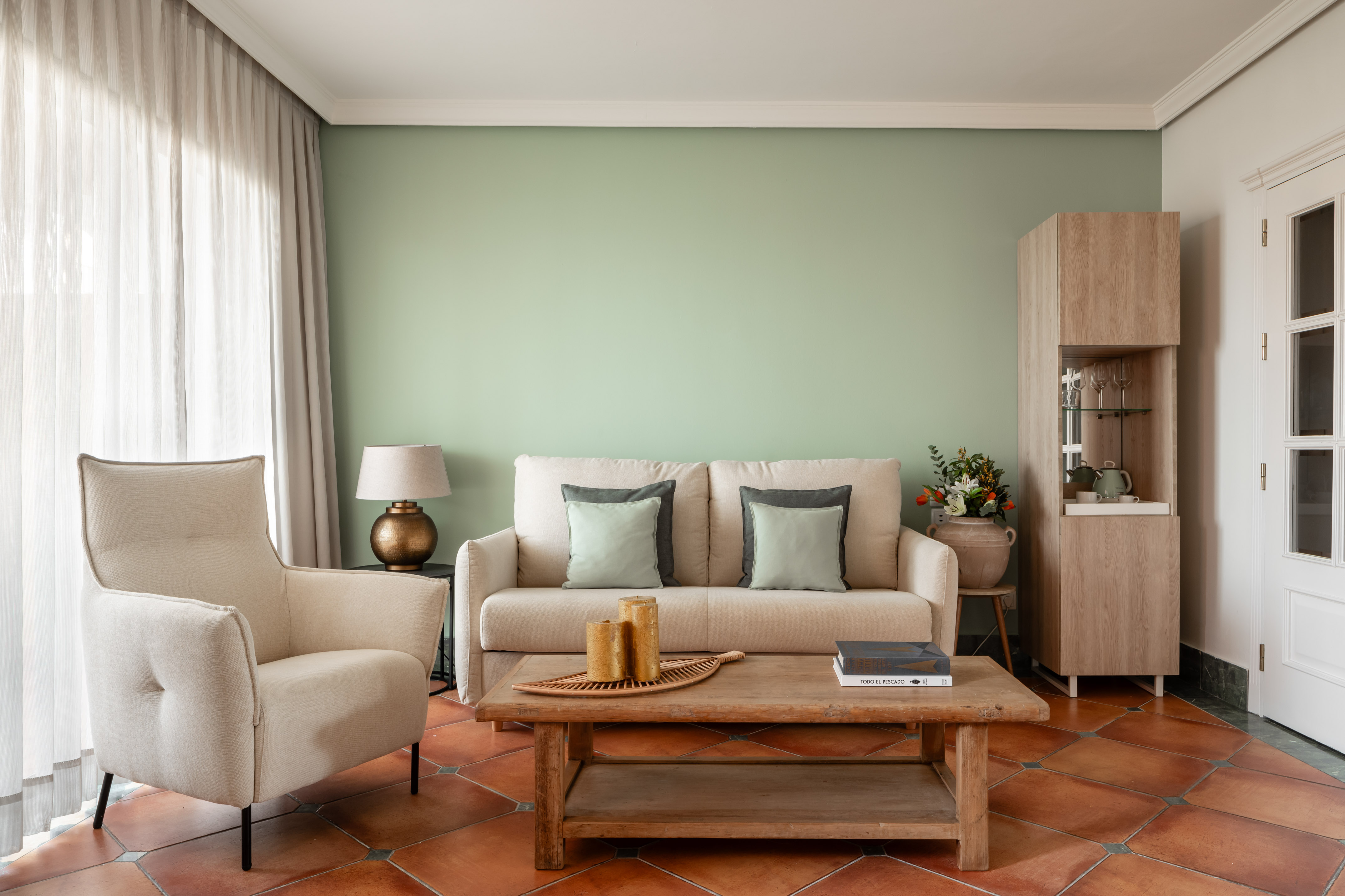 Cozy living room with green wall, beige sofa, wooden coffee table, terracotta floor.