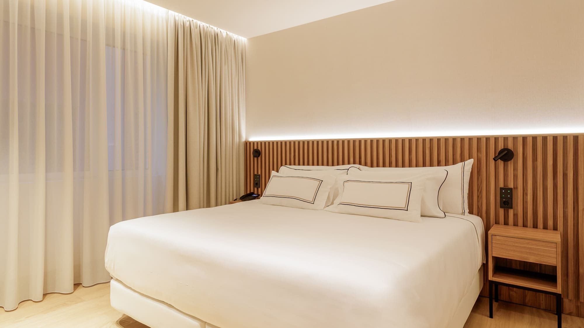 Clean modern hotel bedroom with white bed, wooden headboard, ambient lighting.