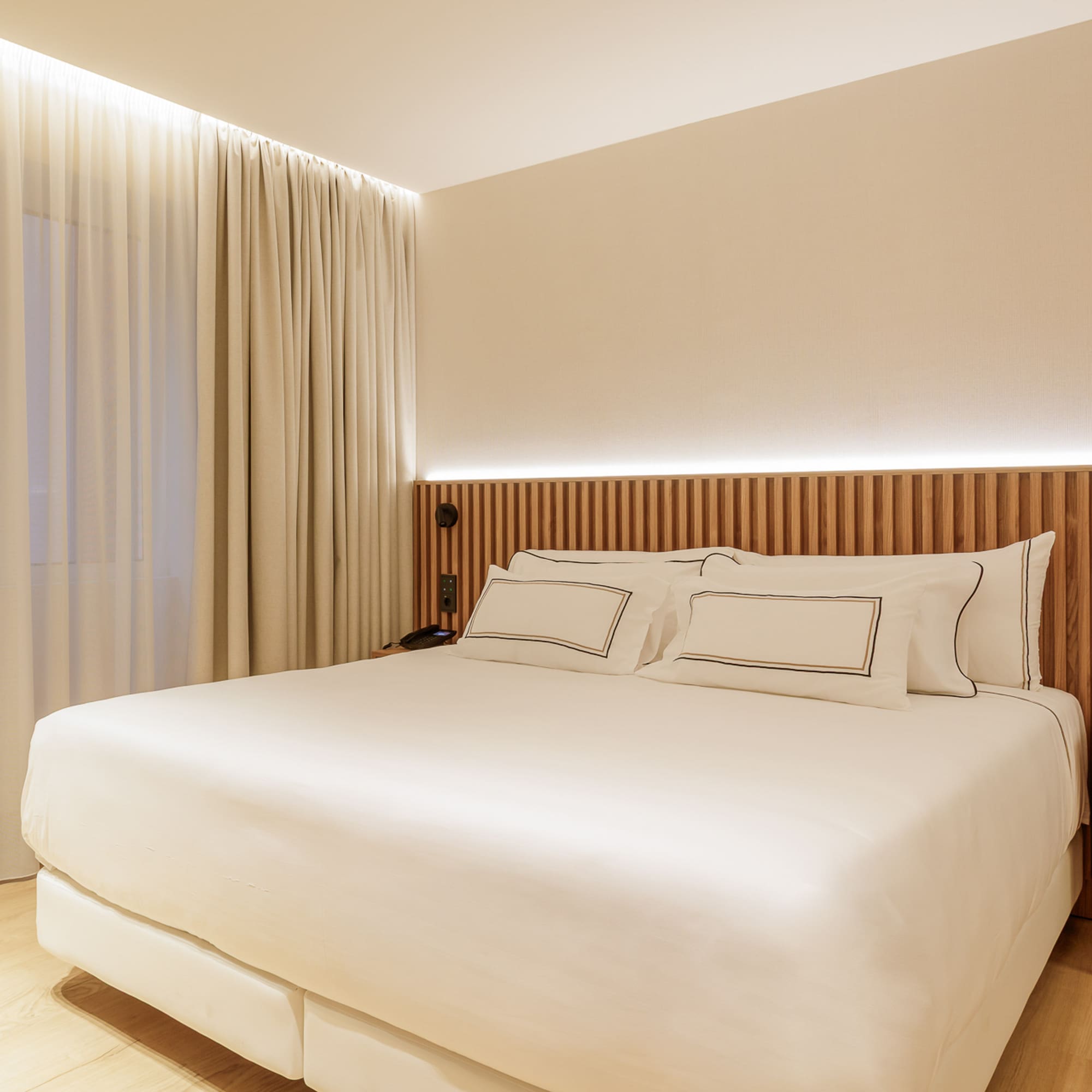 Modern hotel bedroom with large bed, wooden headboard, and soft lighting.