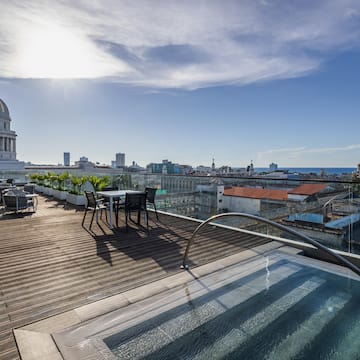 a rooftop with a pool and chairs and a large building with a dome roof