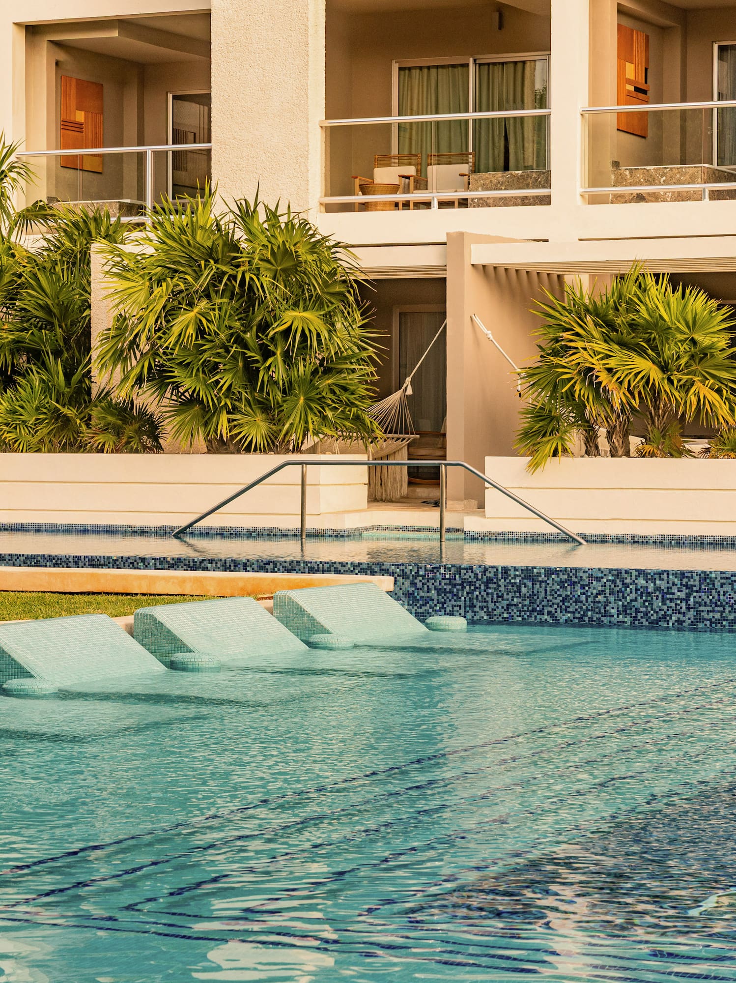 Luxury resort swimming pool with in-water lounge chairs and tropical palm trees.