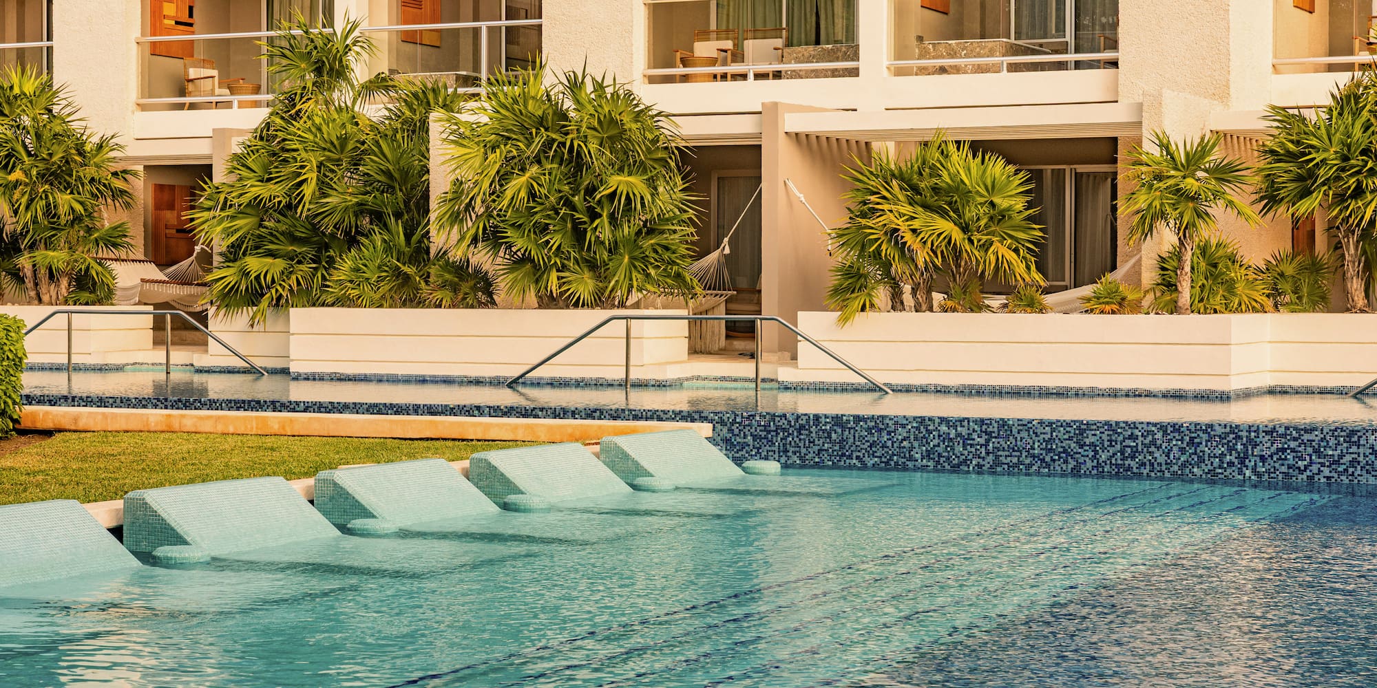Luxury resort swimming pool with in-water lounge chairs and tropical palm trees.