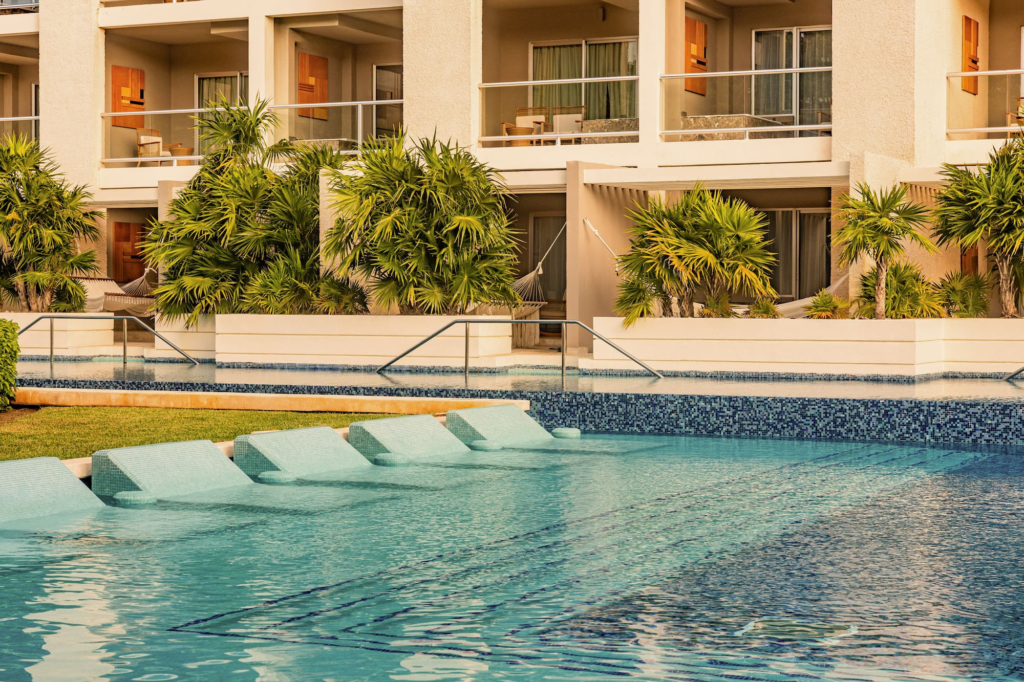Luxury resort swimming pool with in-water lounge chairs and tropical palm trees.