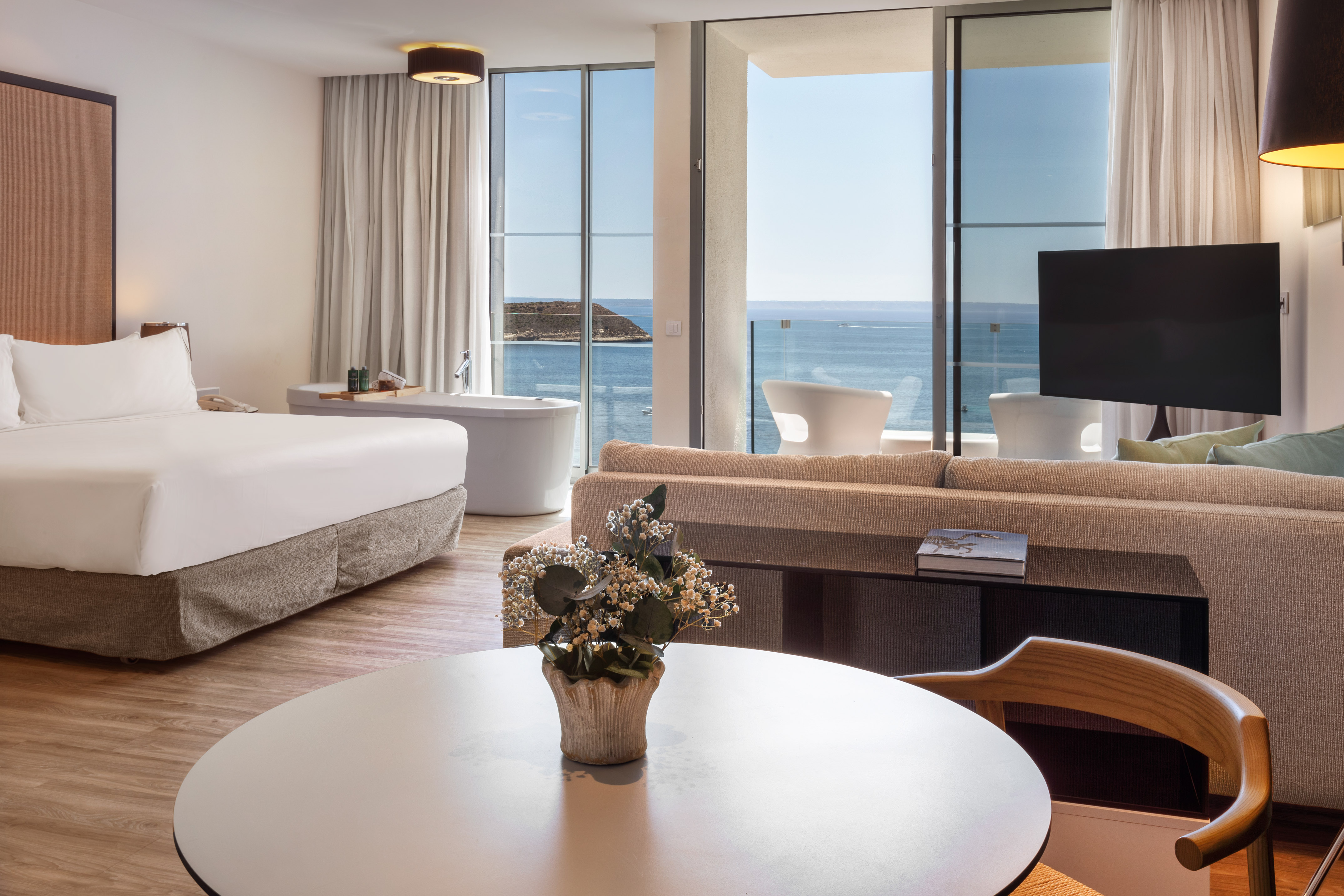 Luxury hotel suite with ocean view, king bed, bathtub, and balcony.
