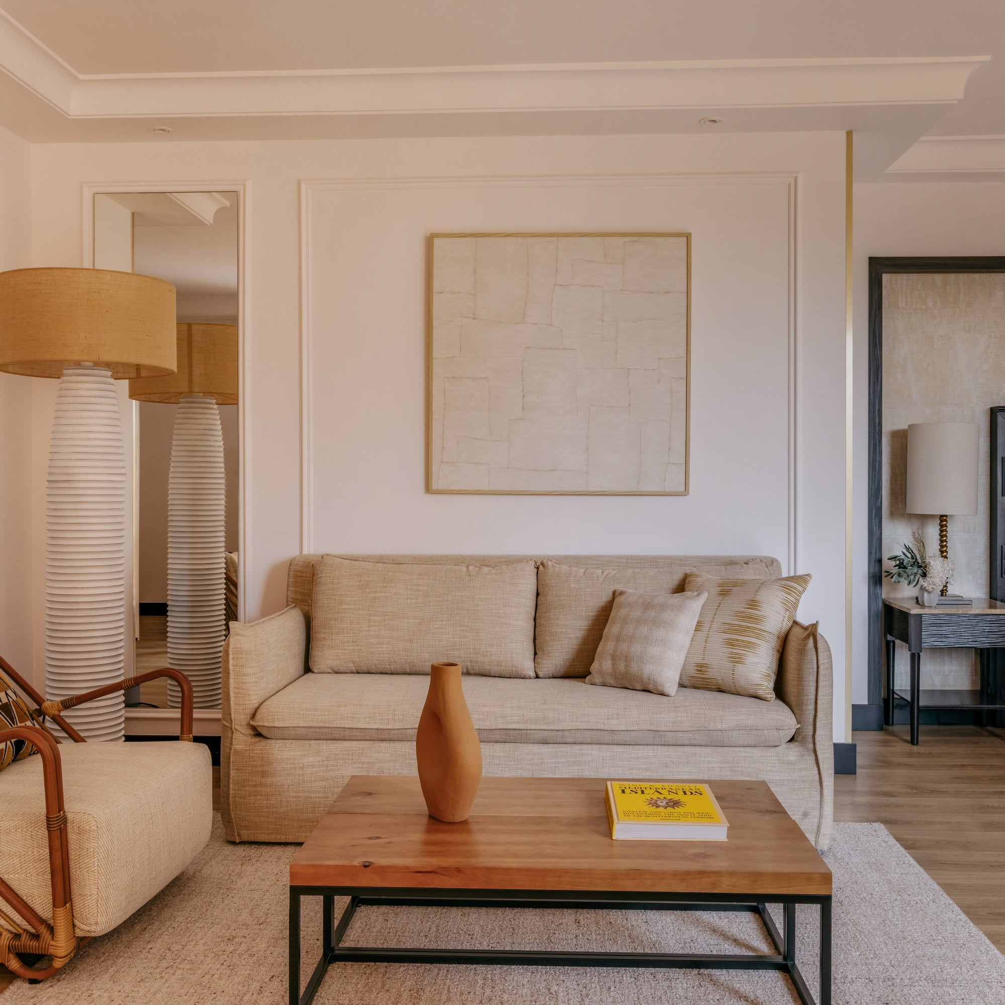 Cozy hotel room with beige sofa, rattan chair, coffee table, and bed.