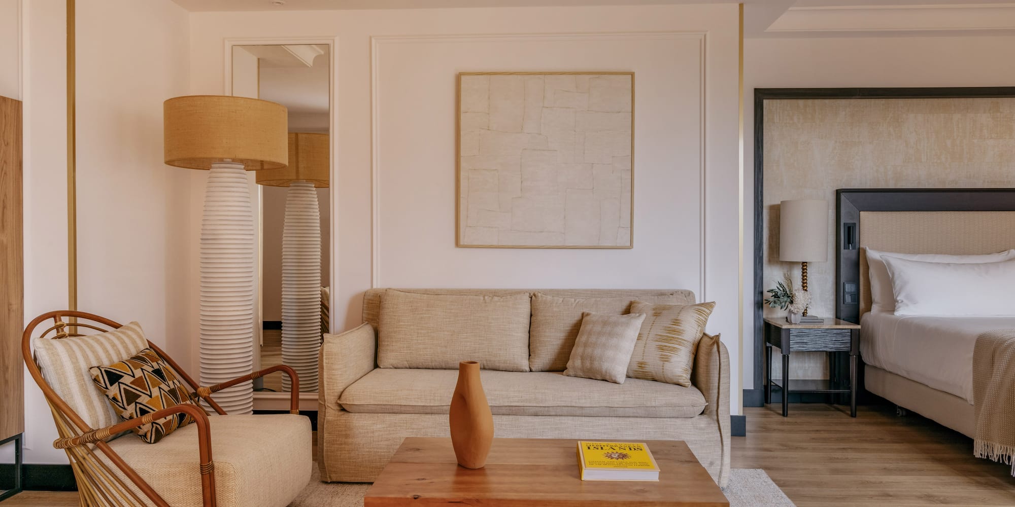 Cozy hotel room with beige sofa, rattan chair, coffee table, and bed.