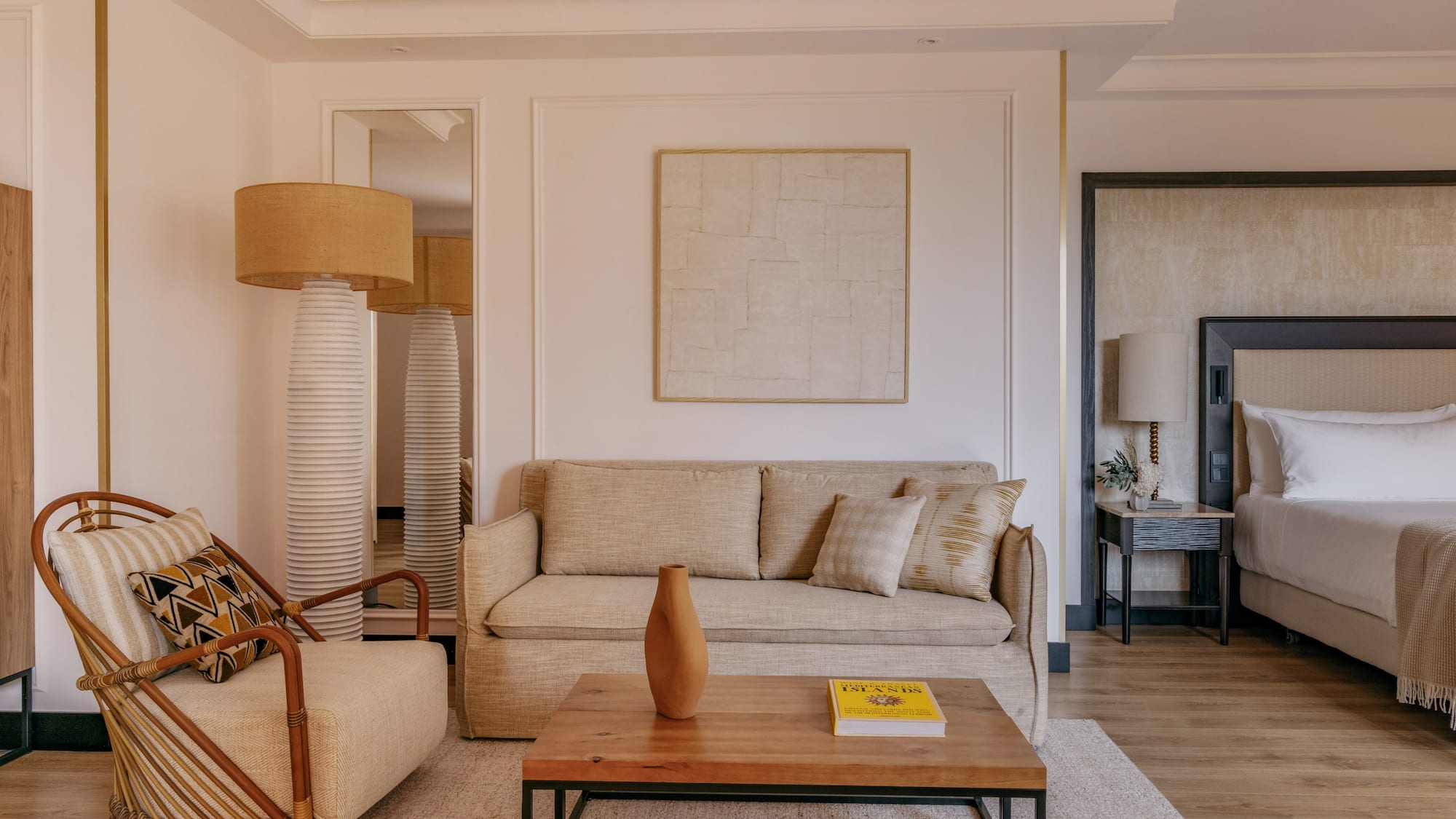 Cozy hotel room with beige sofa, rattan chair, coffee table, and bed.