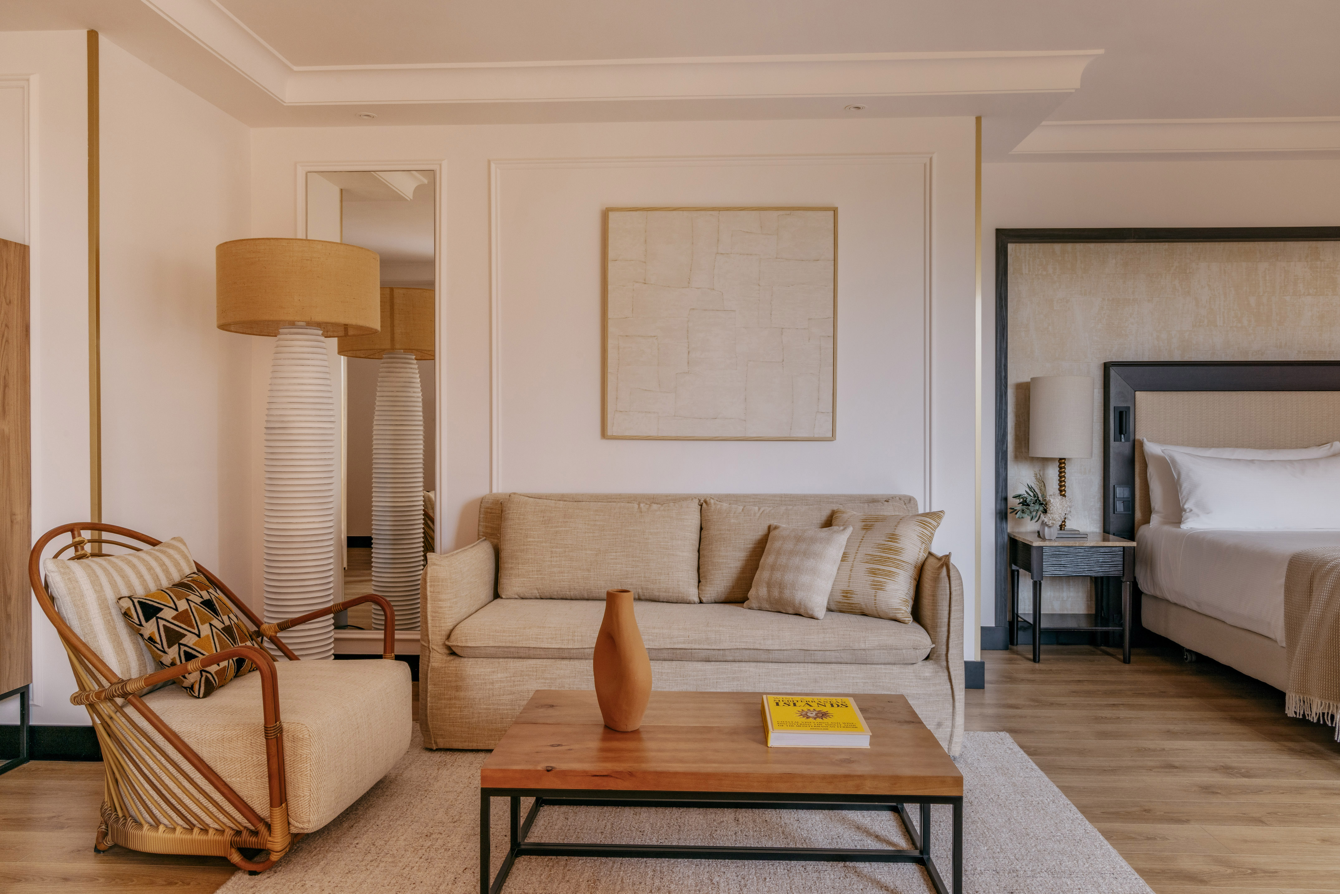 Cozy hotel room with beige sofa, rattan chair, coffee table, and bed.
