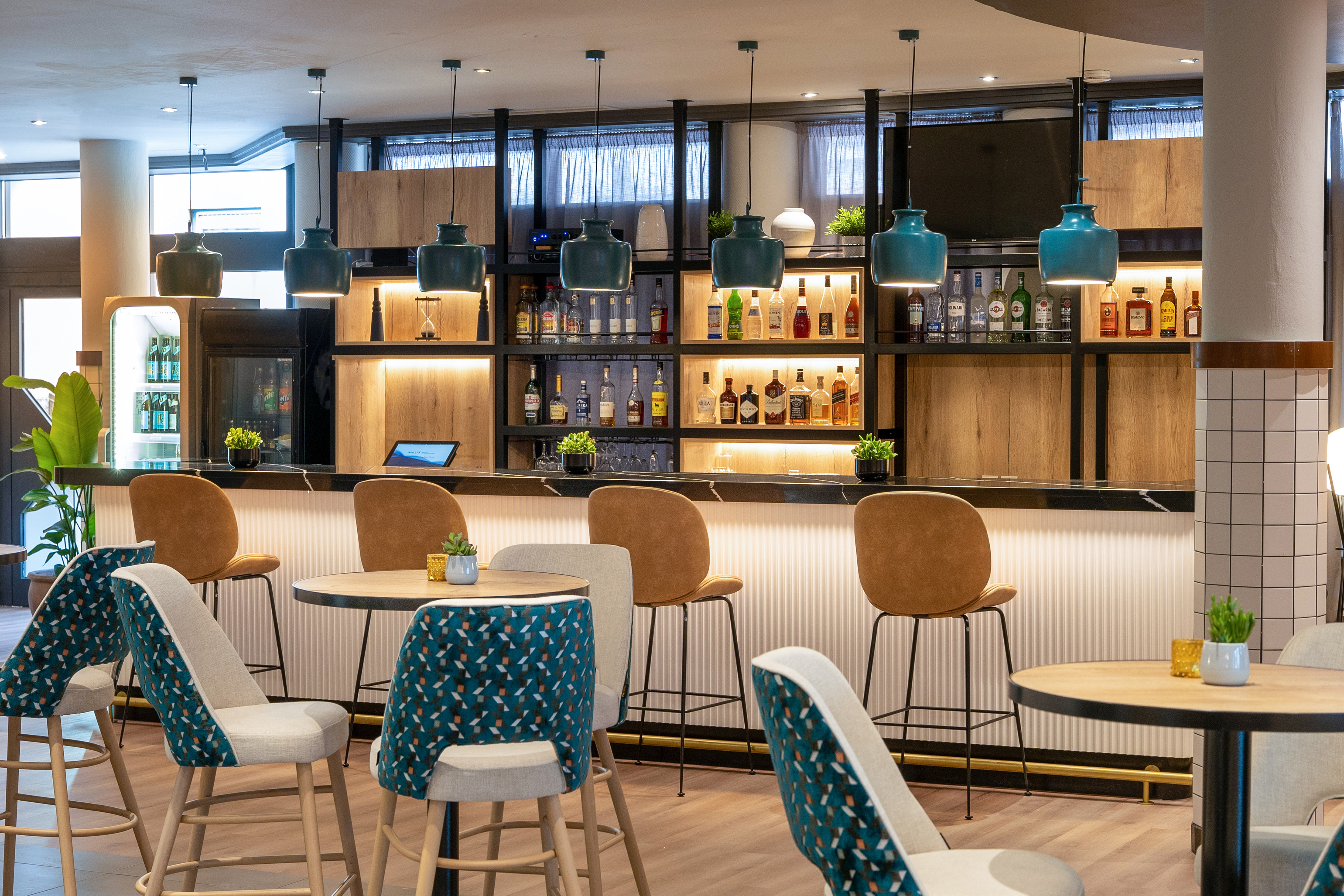Modern hotel bar with stylish counter, bar stools, tables, and illuminated liquor shelves.