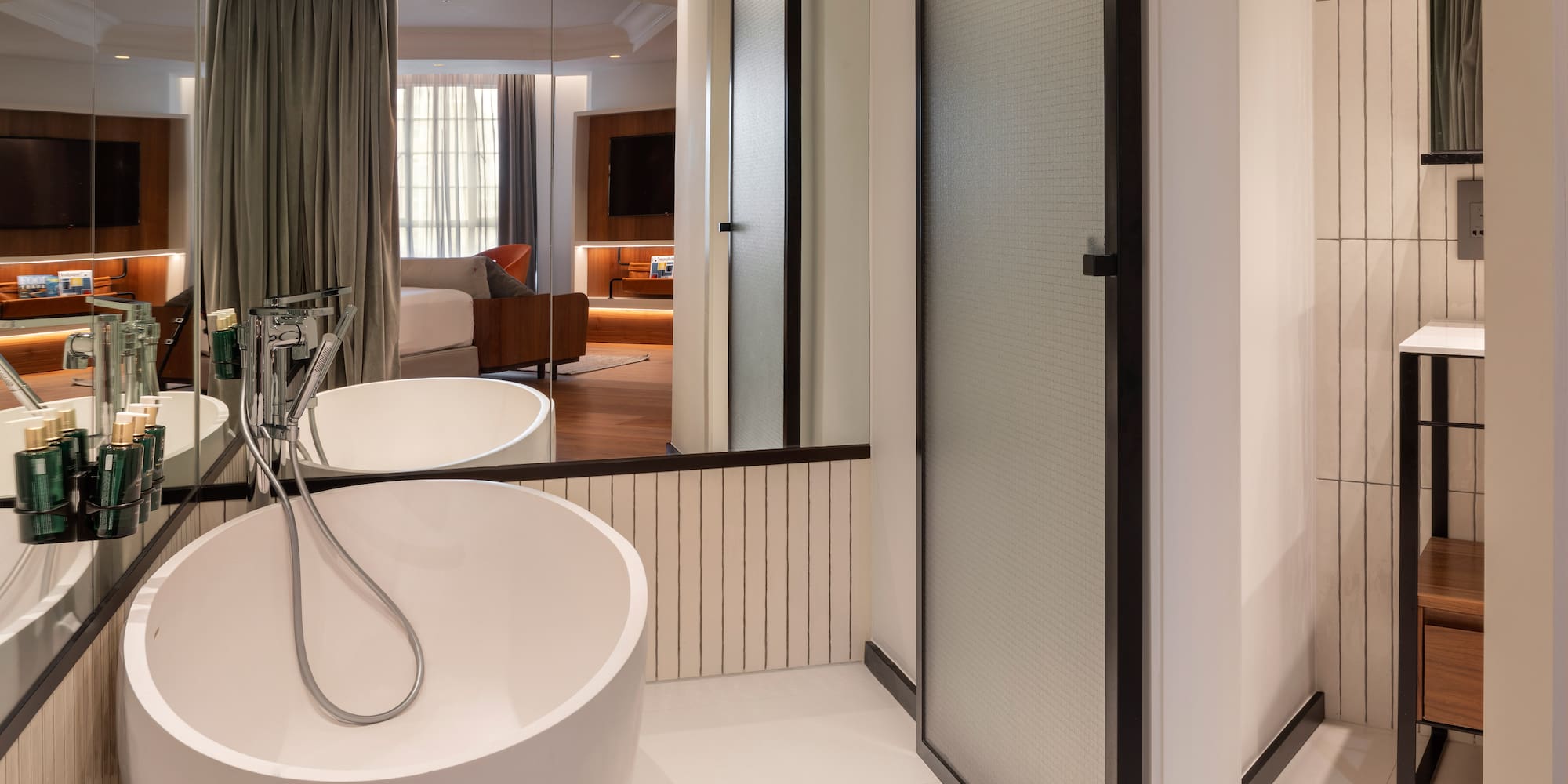 Modern hotel bathroom with freestanding tub, reflecting a stylish bedroom suite.