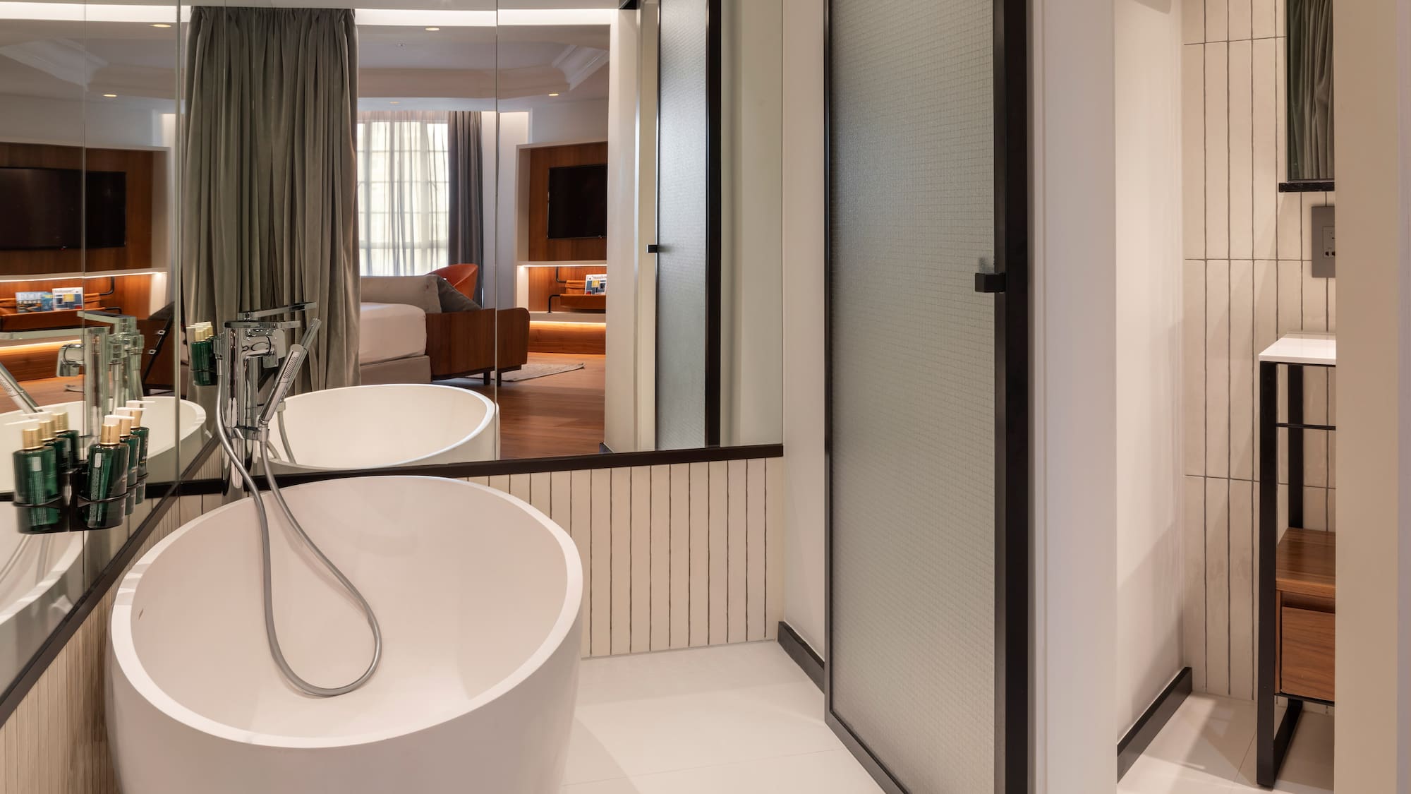 Modern hotel bathroom with freestanding tub, reflecting a stylish bedroom suite.