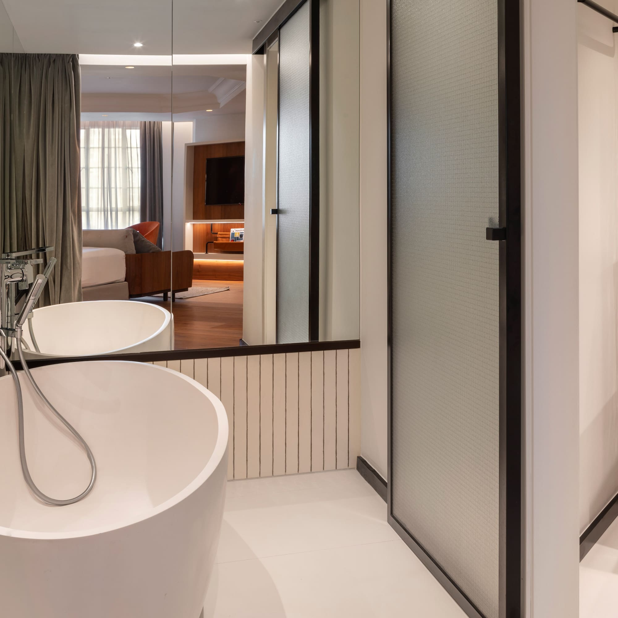 Modern hotel bathroom with freestanding tub, reflecting a stylish bedroom suite.