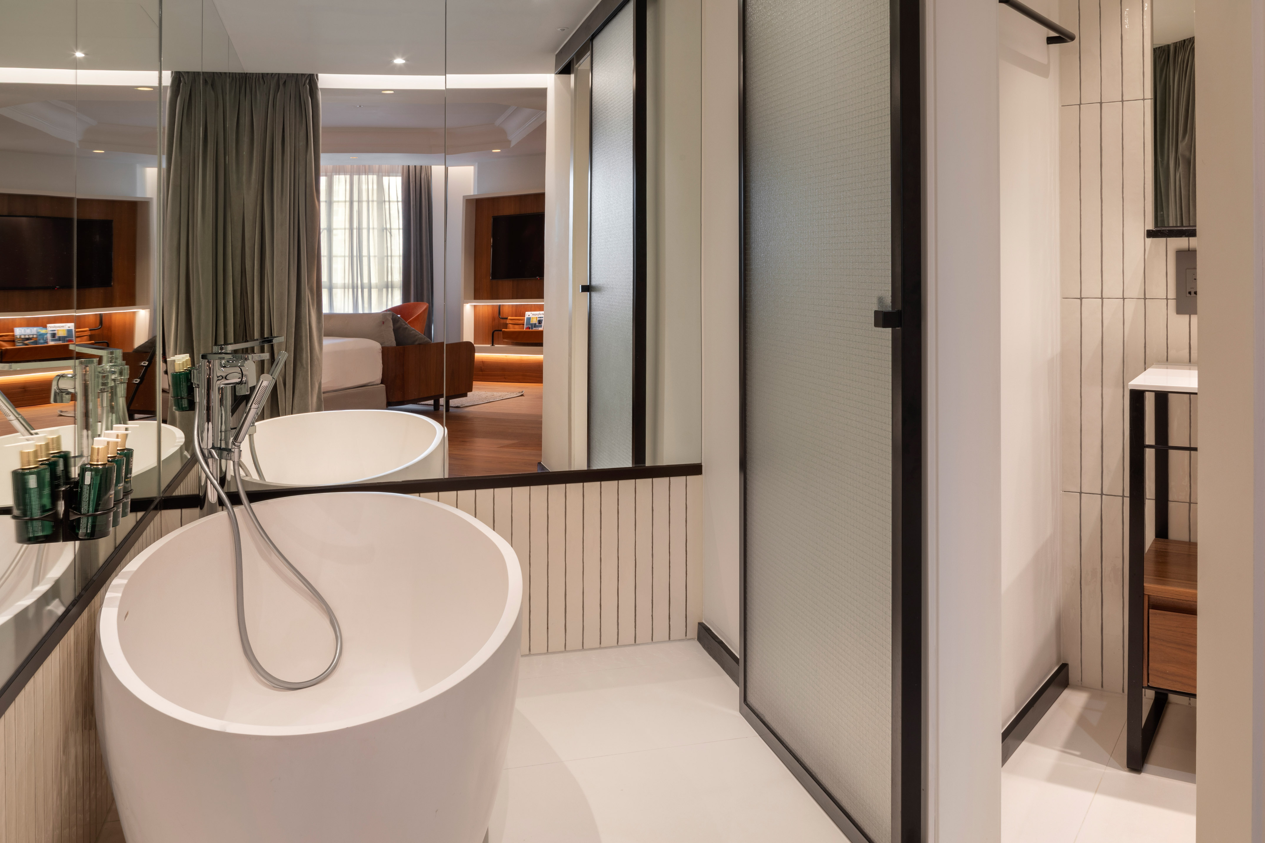 Modern hotel bathroom with freestanding tub, reflecting a stylish bedroom suite.