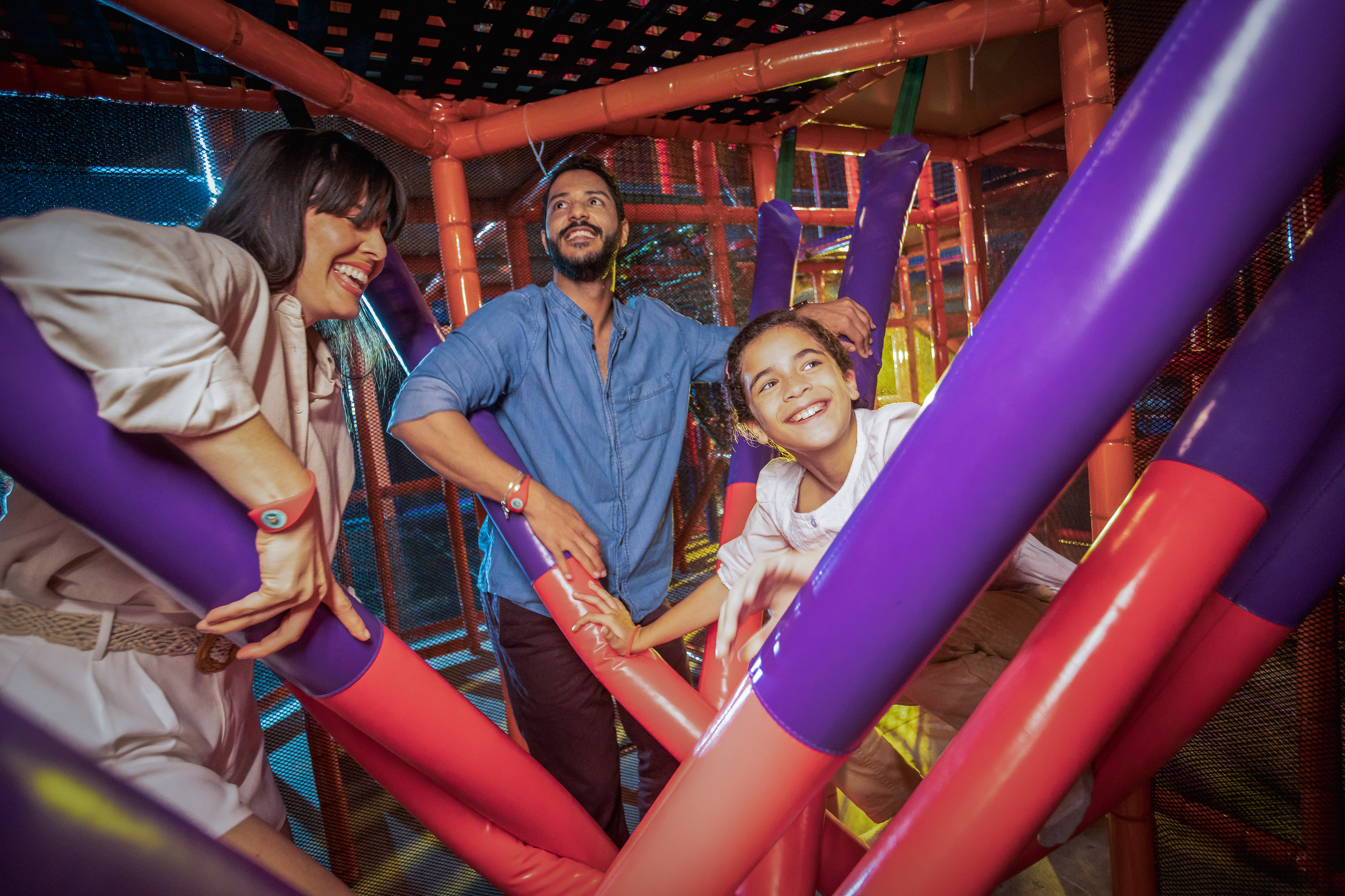 Smiling family enjoying a colorful indoor soft play area.