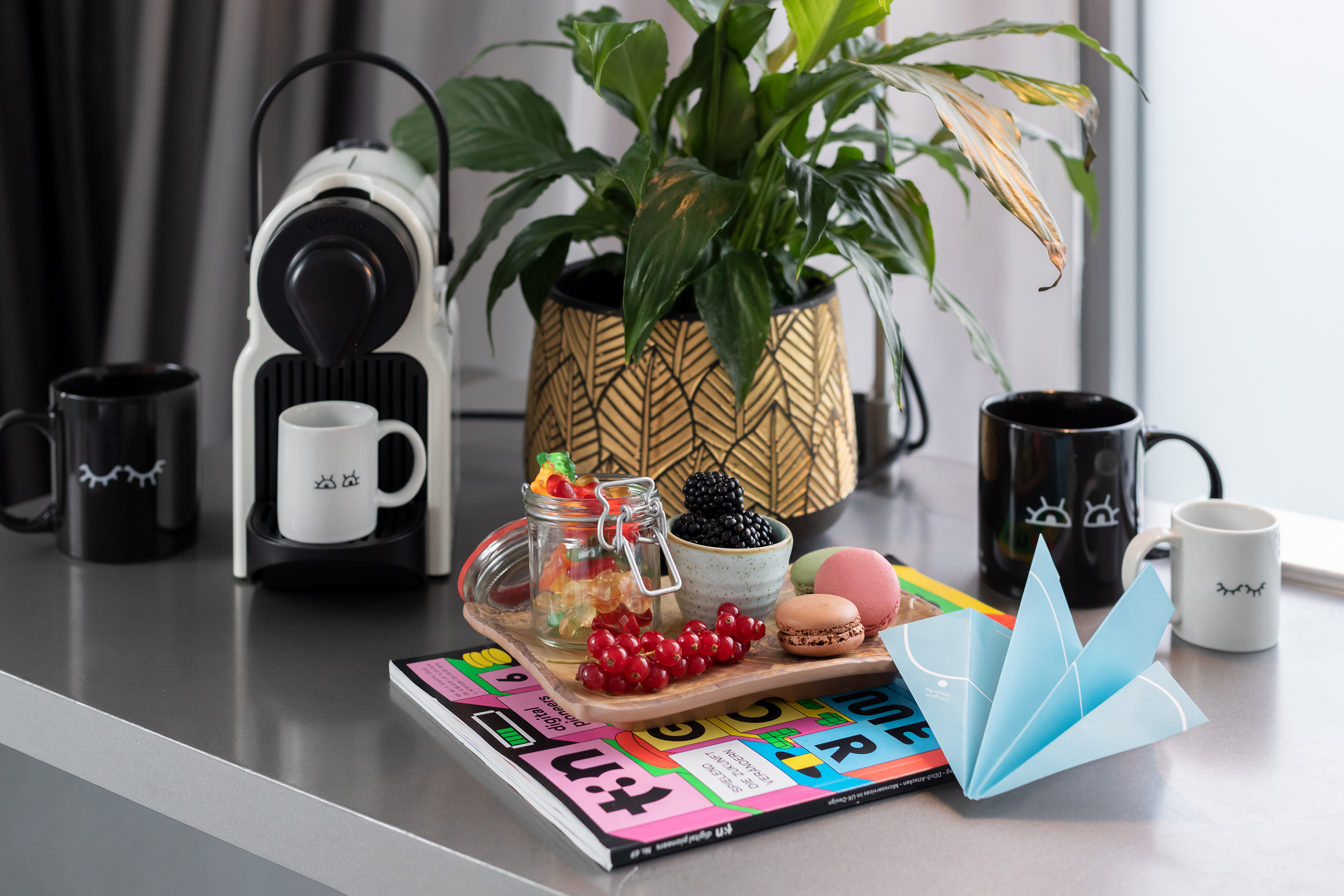 Nespresso machine, mugs, plant, macarons, berries, and gummy candies.