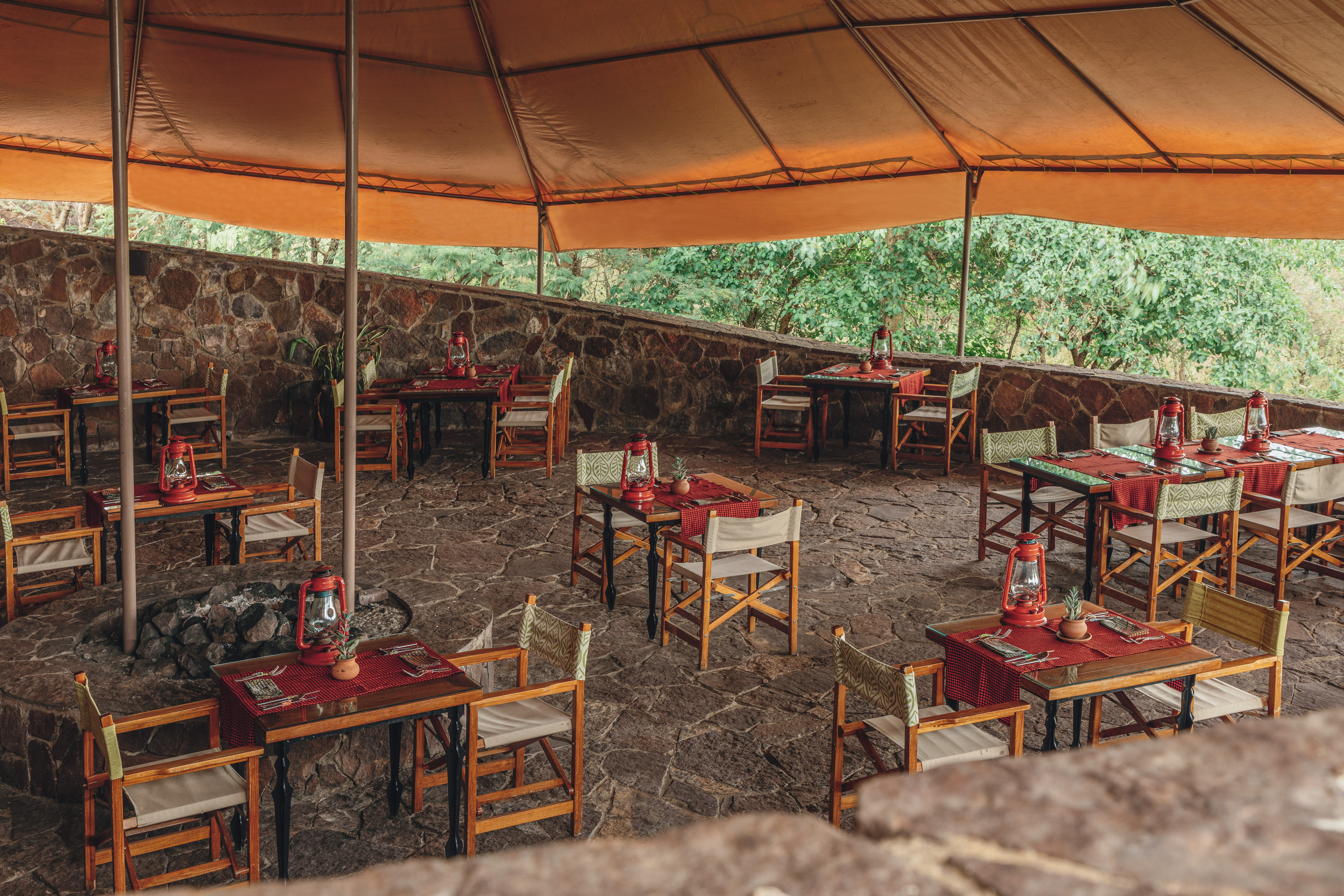 Safari lodge outdoor restaurant, tables with red lanterns under orange canopy.