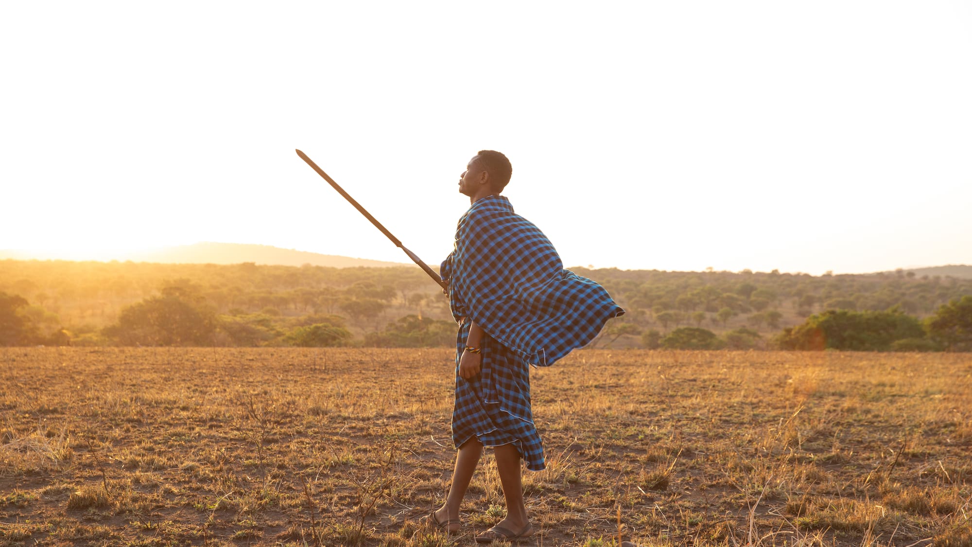 a man in a blue and white plaid robe holding a stick in a field