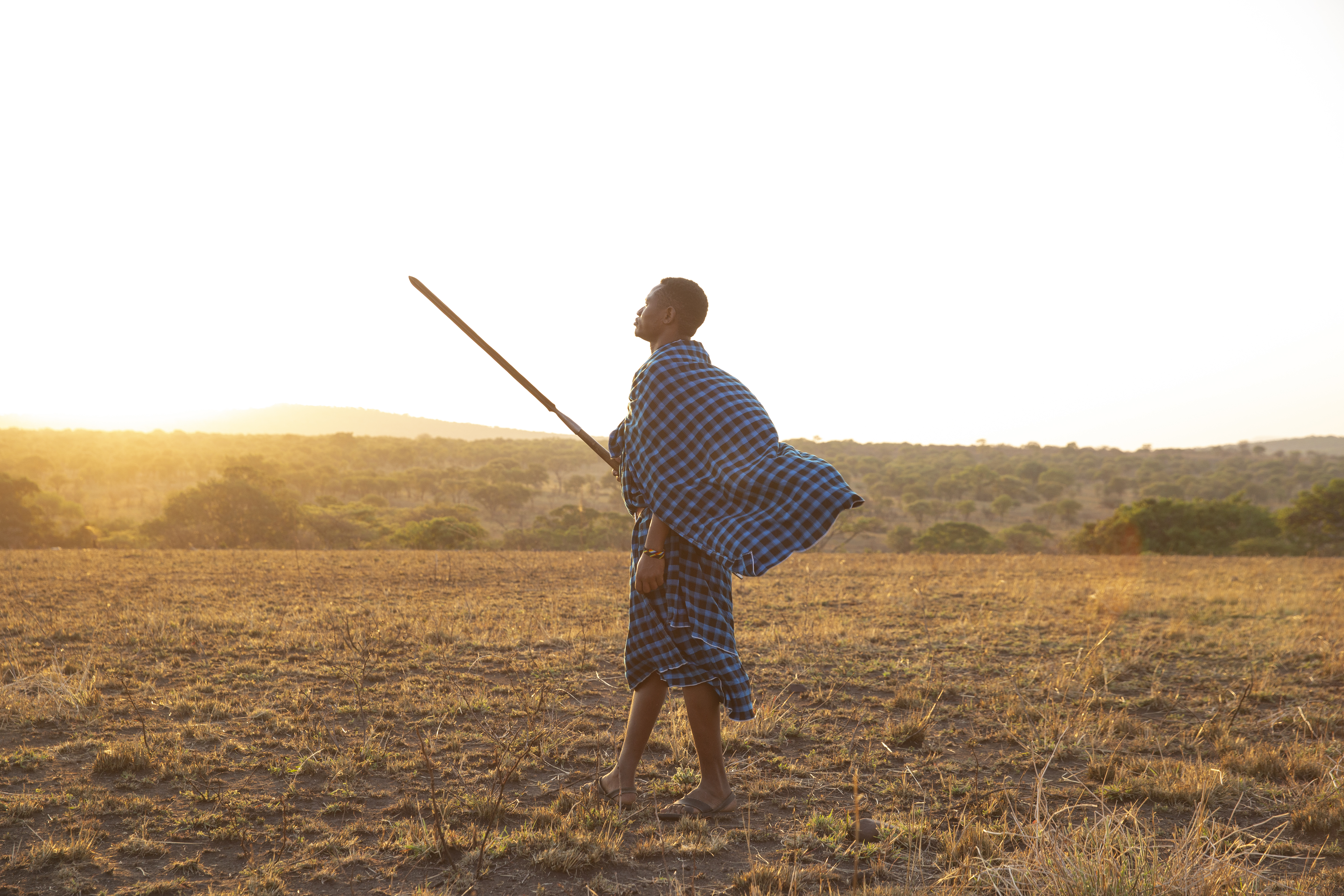 a man in a blue and white plaid robe holding a stick in a field