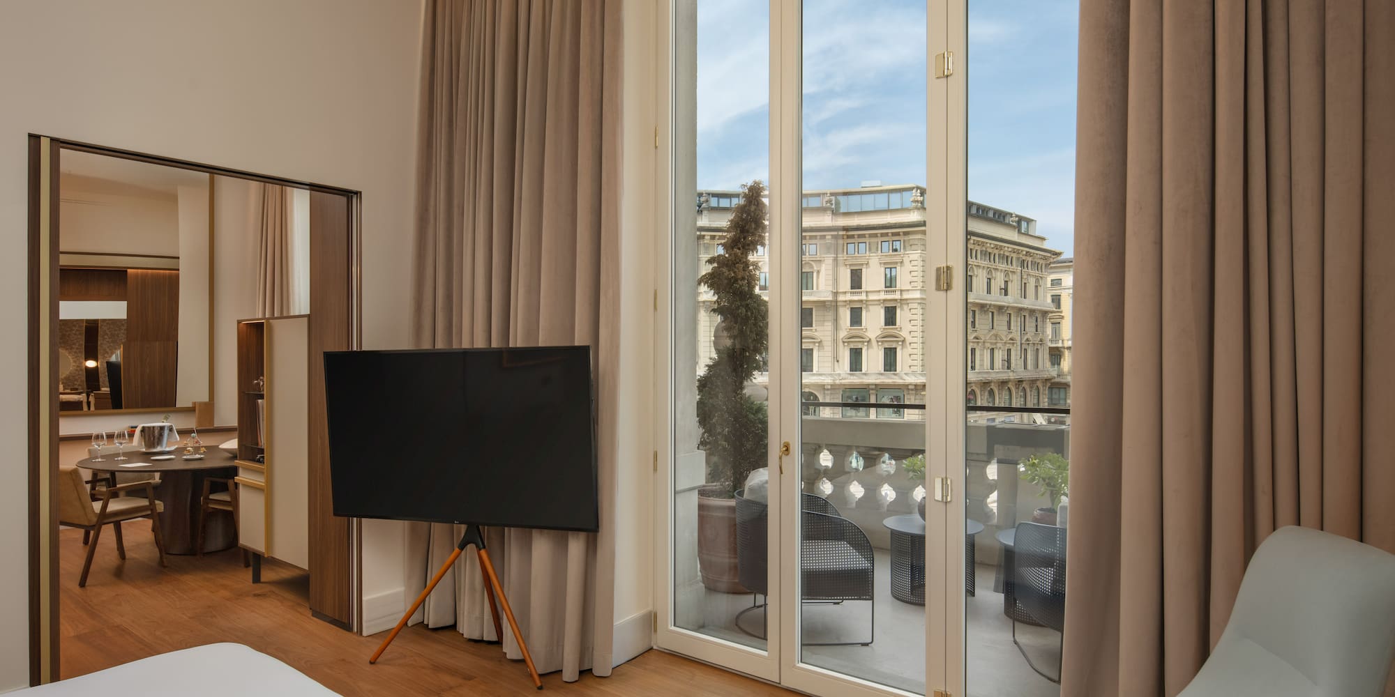 Modern hotel suite with balcony, outdoor seating, and city view.