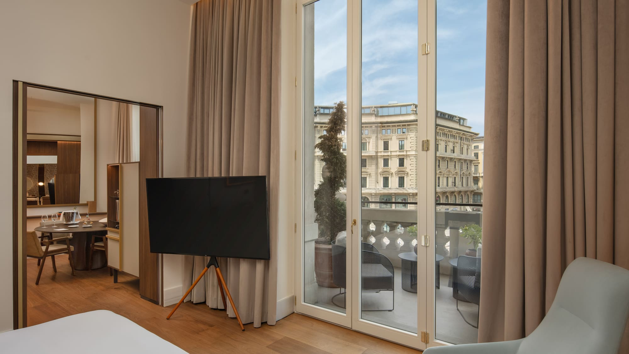 Modern hotel suite with balcony, outdoor seating, and city view.