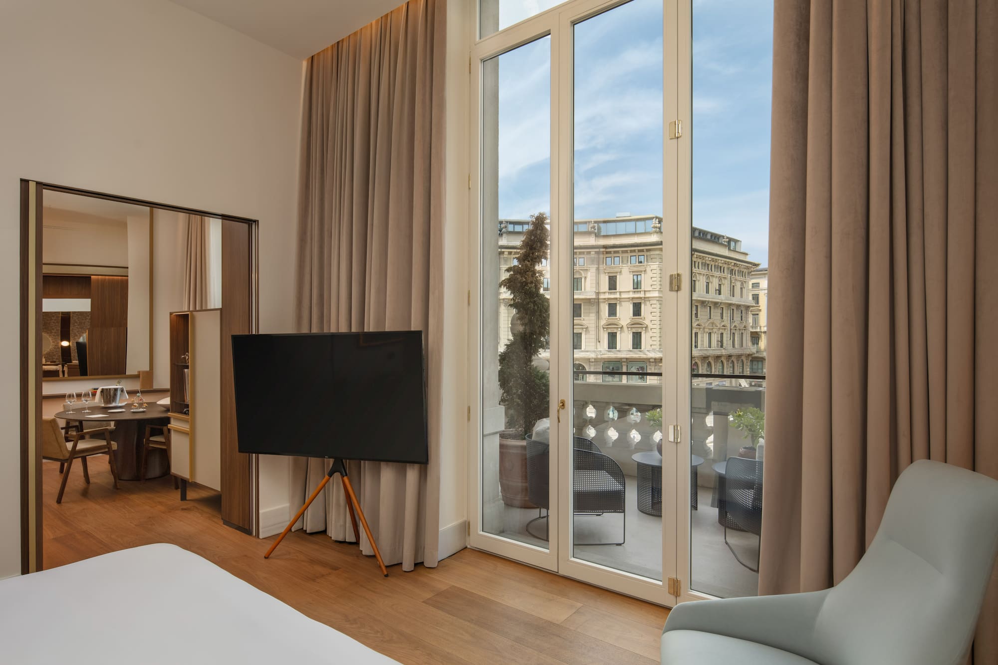 Modern hotel suite with balcony, outdoor seating, and city view.