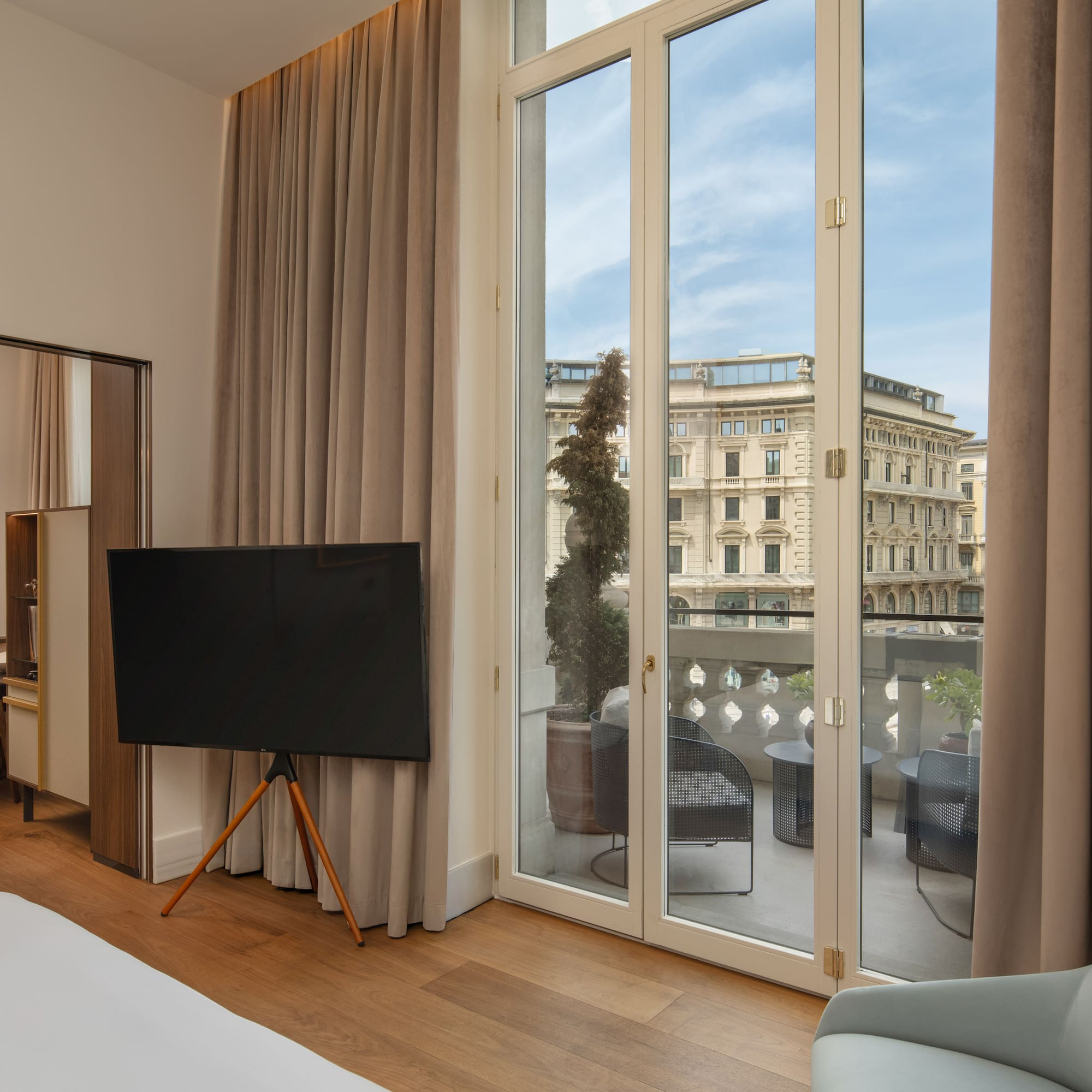 Modern hotel suite with balcony, outdoor seating, and city view.