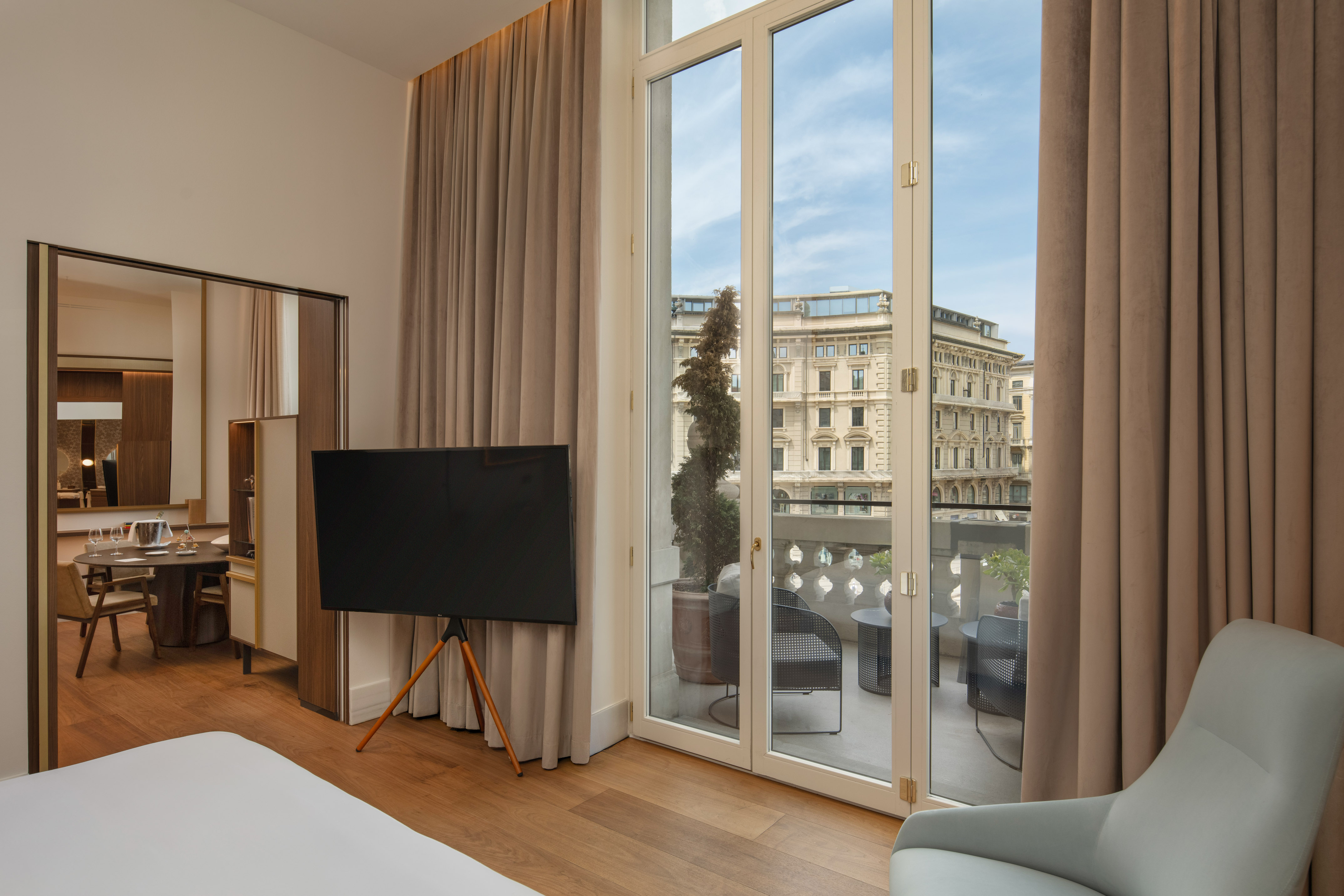 Modern hotel suite with balcony, outdoor seating, and city view.
