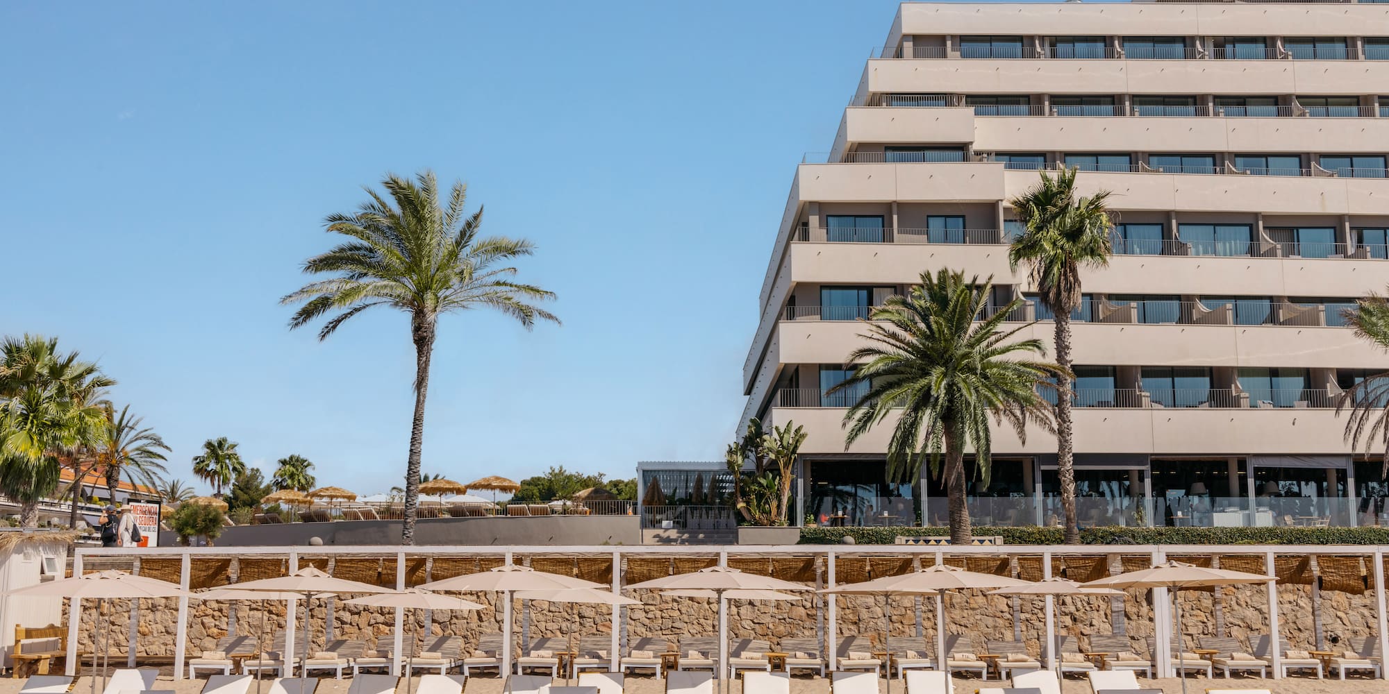 a group of lounge chairs on a beach with palm trees and a building in the background