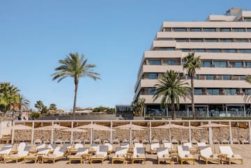 a group of lounge chairs on a beach with palm trees and a building in the background