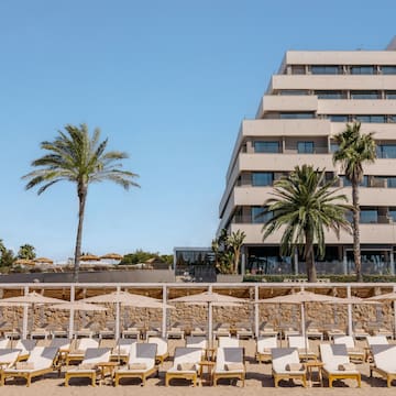 a group of lounge chairs on a beach with palm trees and a building in the background