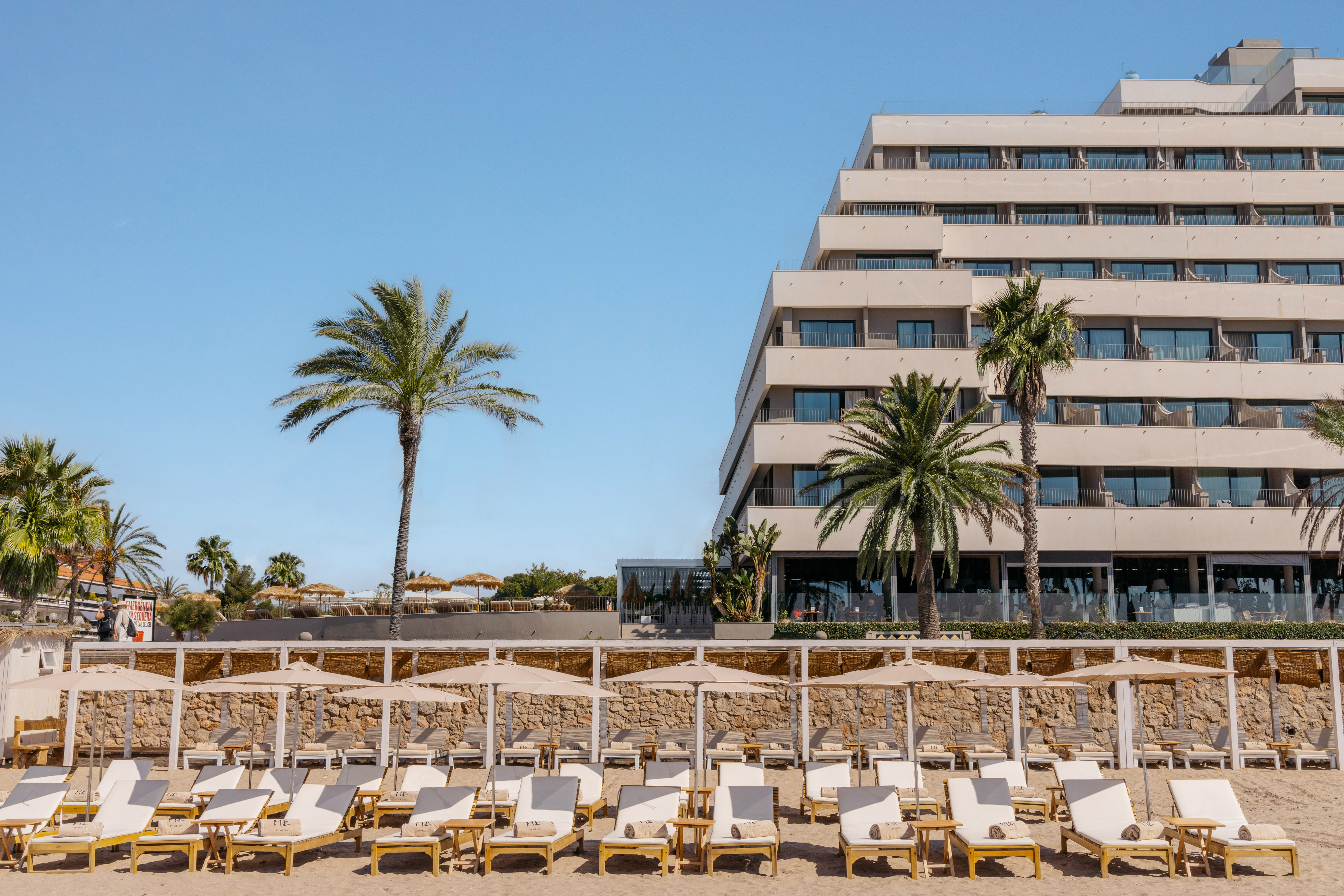 a group of lounge chairs on a beach with palm trees and a building in the background