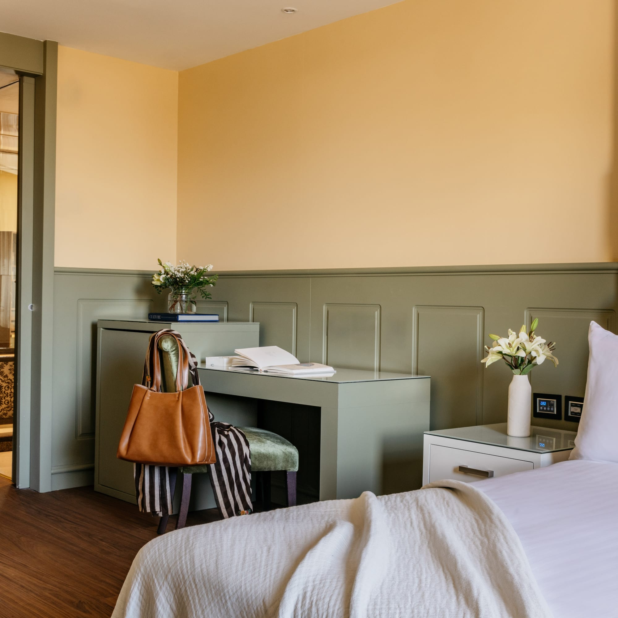 Habitación de hotel elegante con cama, escritorio verde, paredes amarillas y puerta de baño.