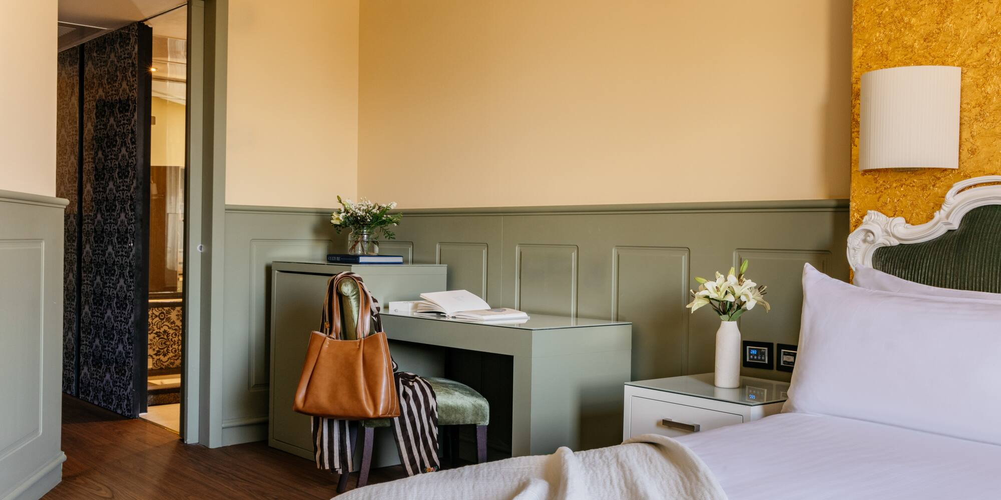 Habitación de hotel elegante con cama, escritorio verde, paredes amarillas y puerta de baño.